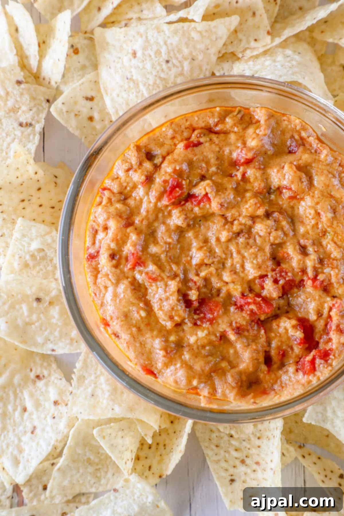 Decadent Smoked Chorizo Queso 5 A glass bowl of smoked chorizo queso dip surrounded by tortilla chips on a light wooden surface.