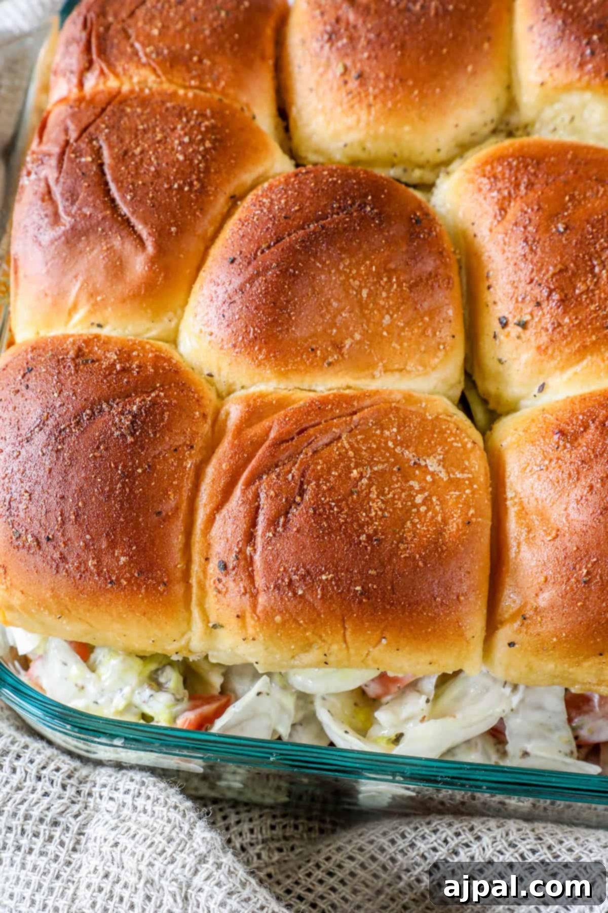 A close-up of a baked dish with golden-brown rolls on top and visible creamy filling, placed in a glass baking dish.