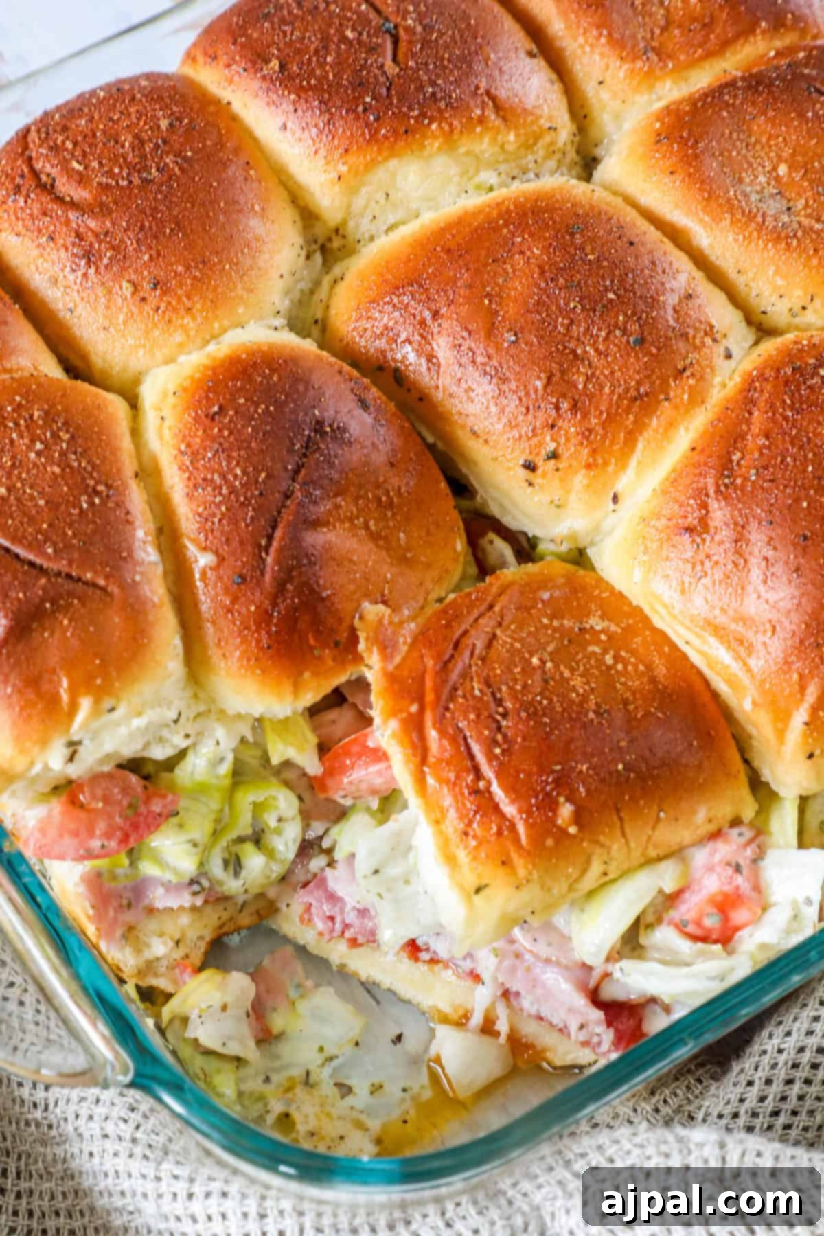 A glass baking dish with a batch of baked sliders filled with lettuce, tomato, and bacon.