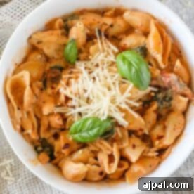 A bowl of creamy pasta with shell noodles, topped with grated cheese and basil leaves, tempting and delicious.