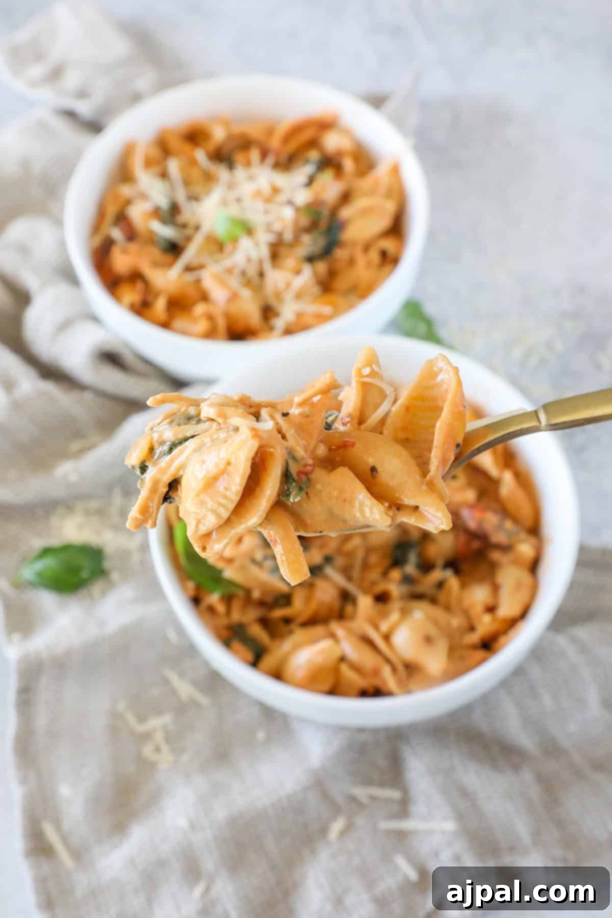 Two enticing bowls of creamy pasta shells, generously topped with fresh herbs and grated cheese. A fork hovers over one bowl, ready for a taste.