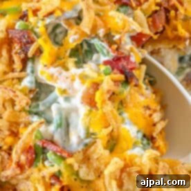 A close-up of a cheesy green bean casserole showcases crispy fried onions and savory bacon pieces atop a creamy sauce, with a spoon ready to serve.