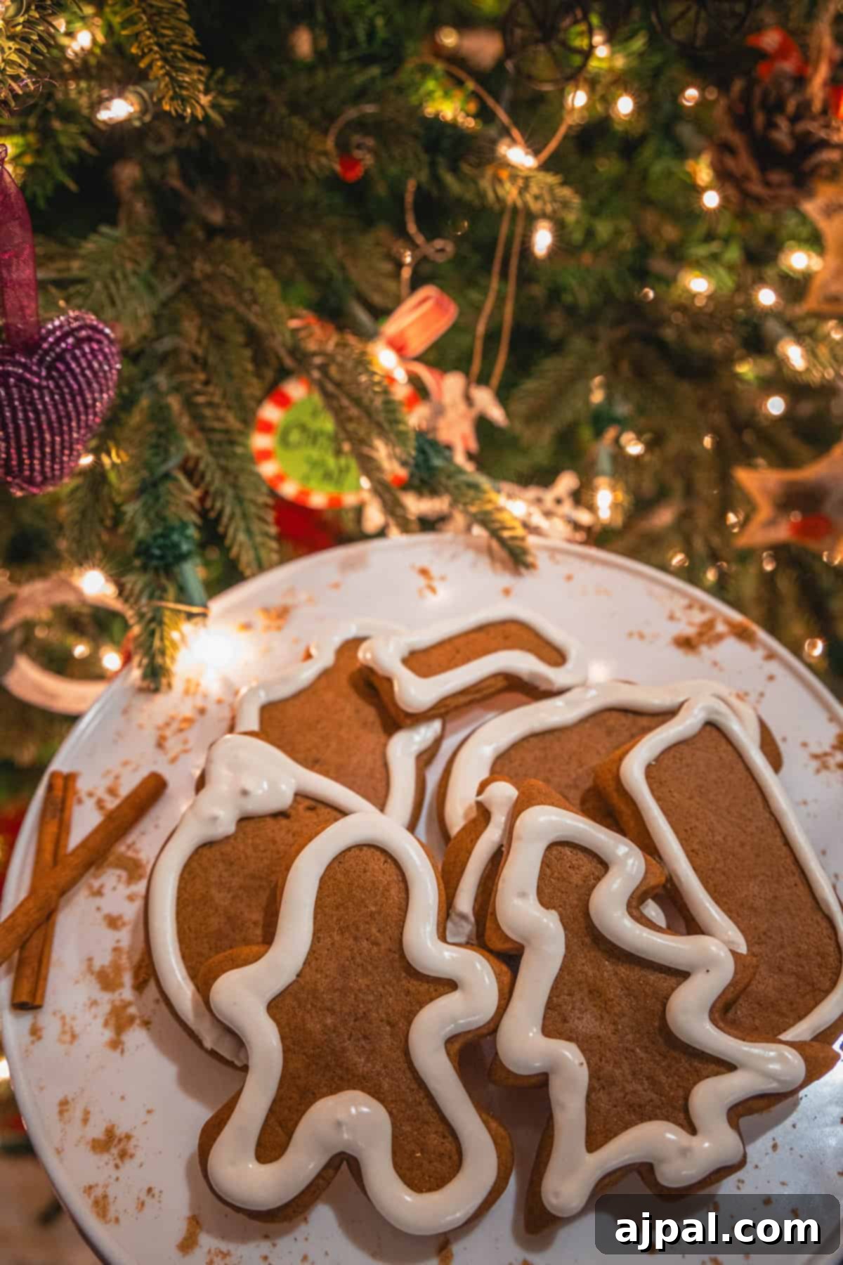 Perfectly Spiced Gingerbread 3 A charming plate of gingerbread cookies, intricately iced and shaped, sits elegantly near a resplendent Christmas tree adorned with twinkling lights and festive ornaments.