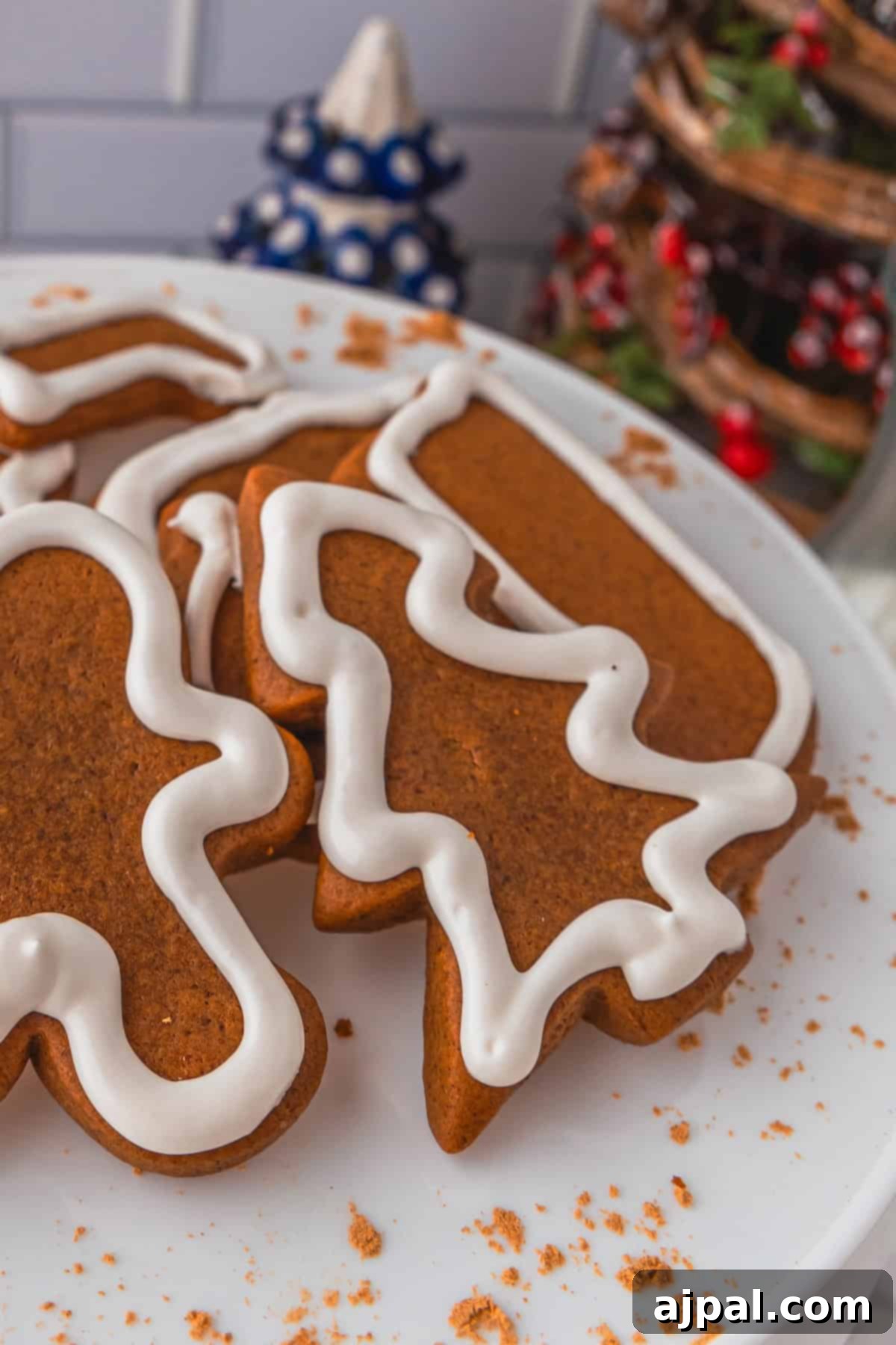 Perfectly Spiced Gingerbread 5 Gingerbread cookies with white icing in tree, candy cane, and gingerbread person shapes rest on a white plate, surrounded by crumbled gingerbread cookie bits.
