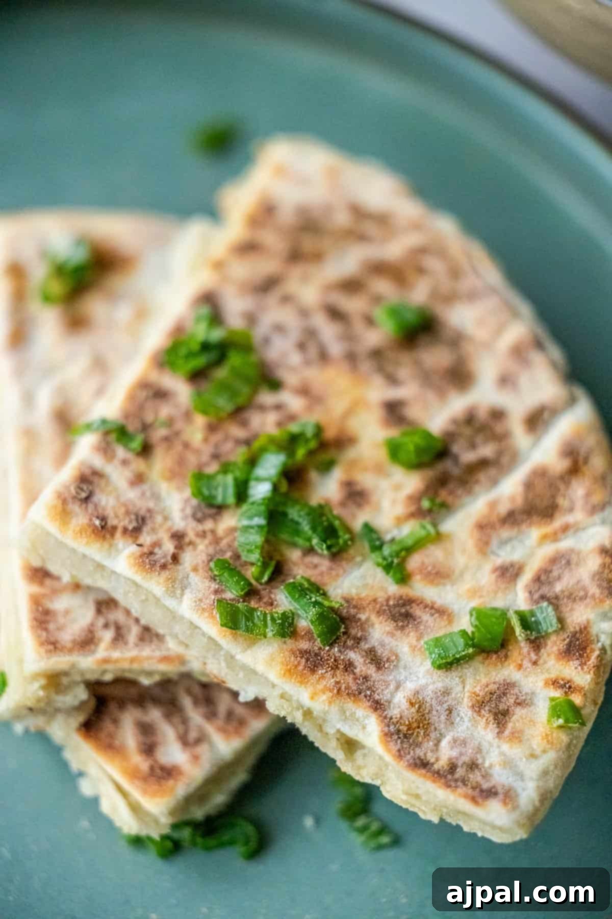 Classic Scottish Tattie Scones 2 Sliced scallion pancakes on a green plate, reminiscent of Scottish tattie scones, topped with a sprinkle of chopped green onions.