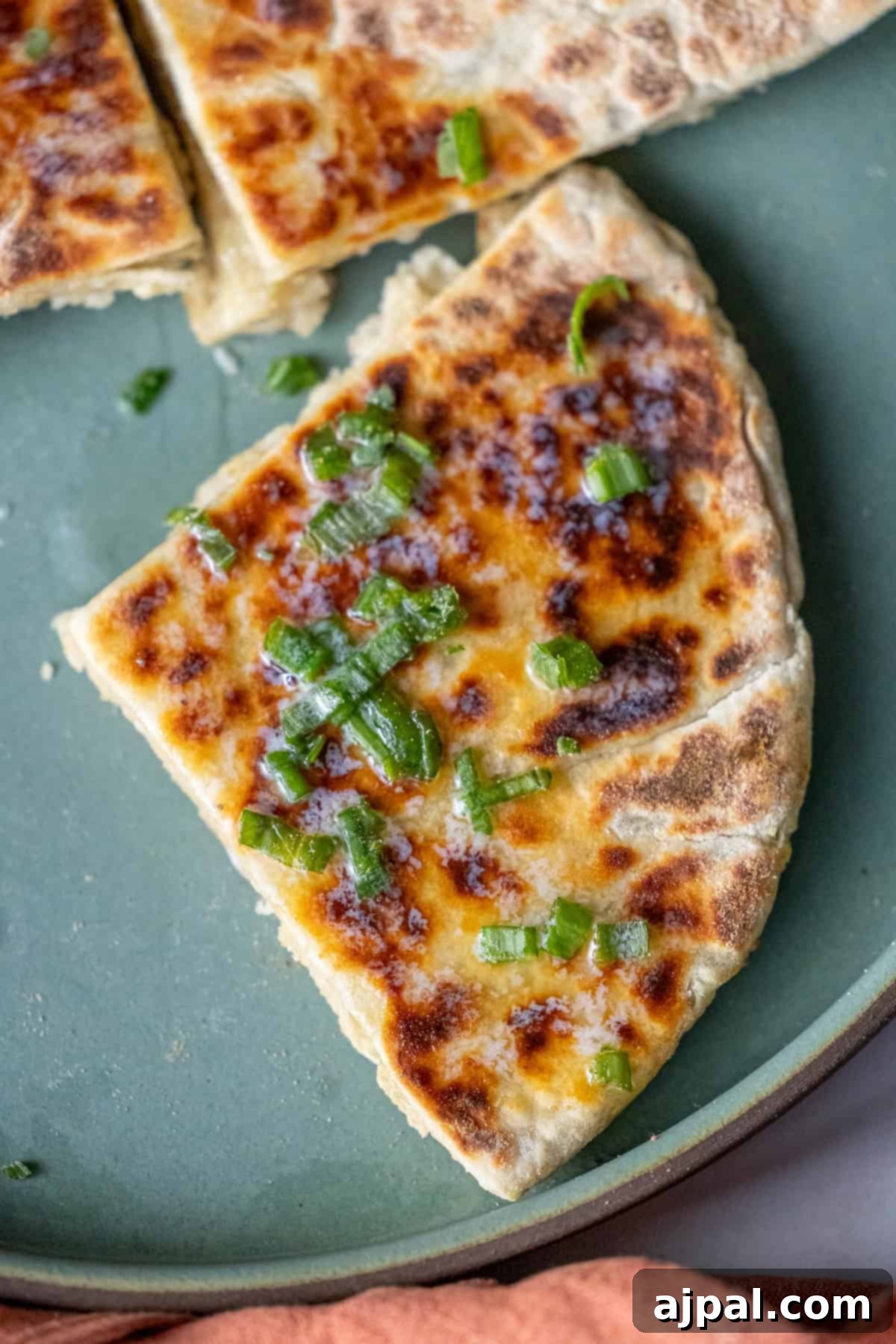 Classic Scottish Tattie Scones 12 A slice of stuffed flatbread, reminiscent of a Scottish tattie scone, is topped with chopped green onions and rests on a green plate.