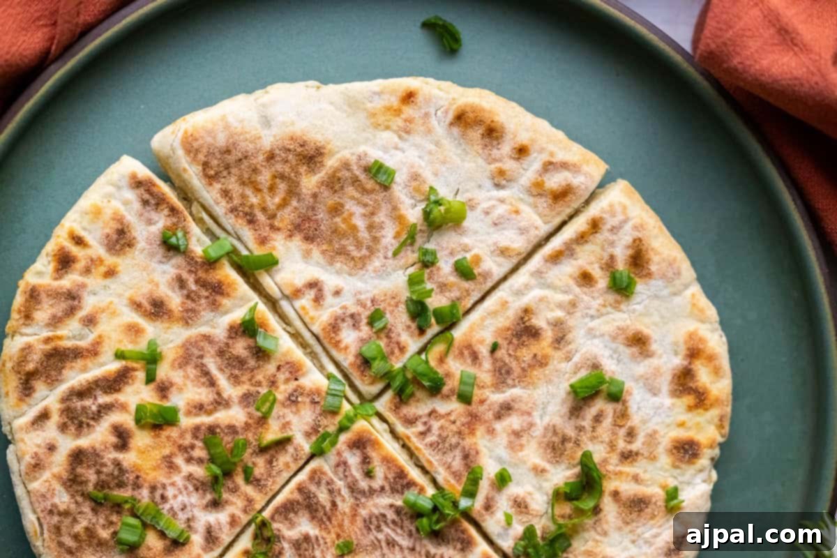 Classic Scottish Tattie Scones 13 A sliced flatbread resembling Scottish tattie scones, topped with chopped green onions, rests on a green plate against an orange fabric background.