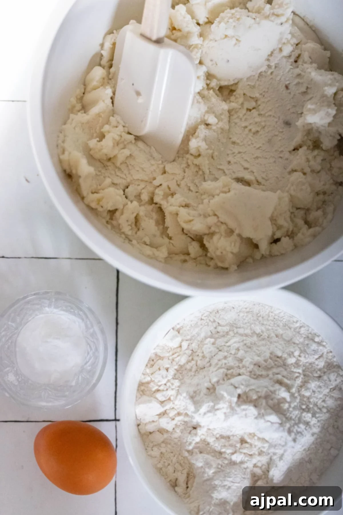 Classic Scottish Tattie Scones 3 Bowls with dough, a spatula, flour, an egg, and a small glass of salt are arranged on a white tiled surface, ready for crafting the perfect Scottish Tattie Scones.