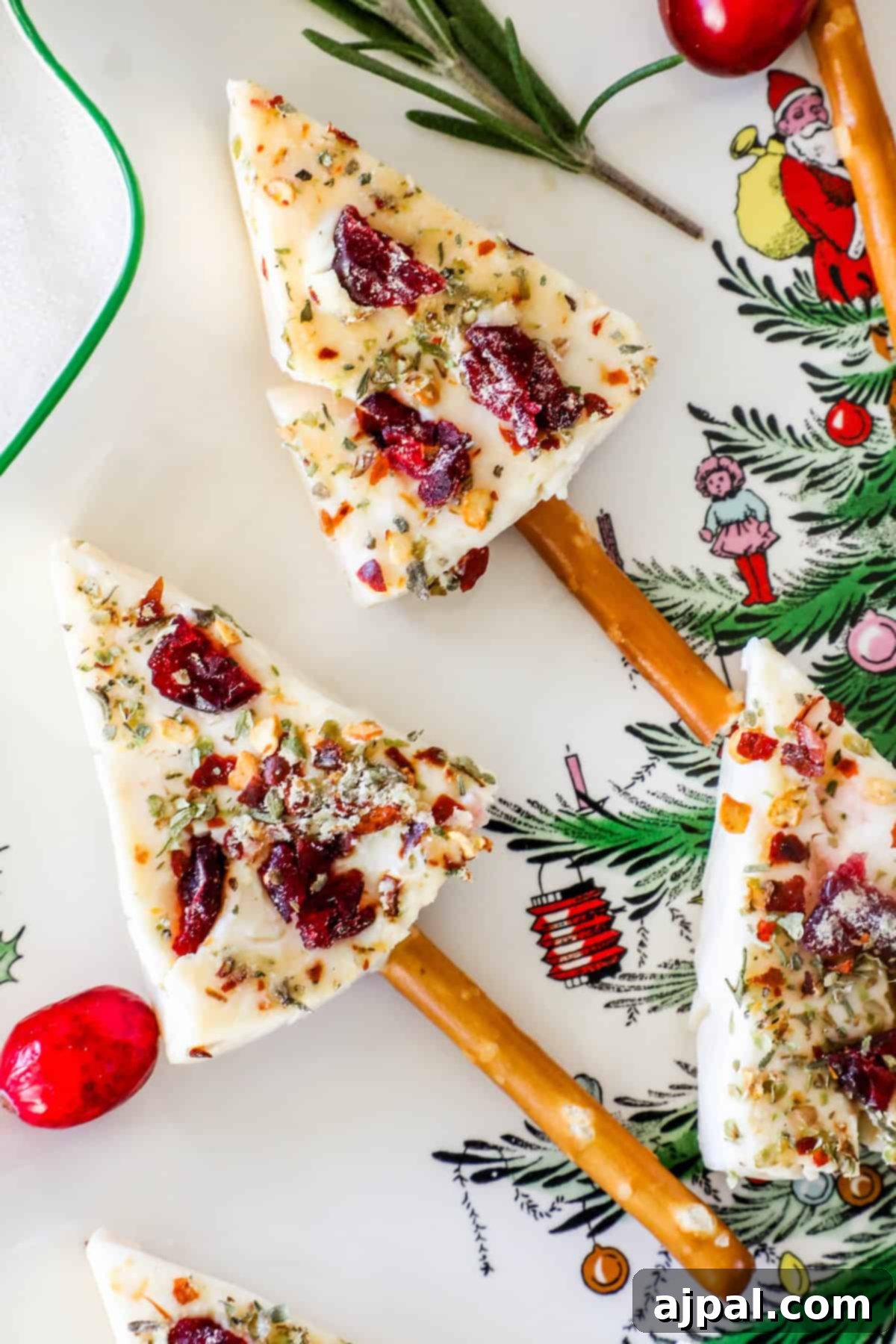 Festive Cheese Tree Bites 3 Festive Christmas tree cheese wedges with cranberries and herbs on pretzel sticks, placed on a holiday-themed plate adorned with festive designs and decorations.