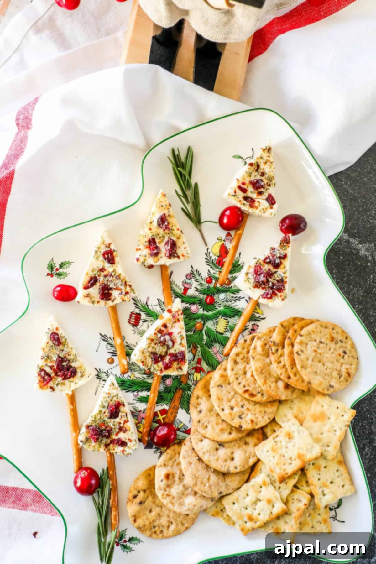Festive Cheese Tree Bites 4 Festive Christmas tree cheese wedges adorned with cranberries and nuts are artfully placed on pretzel sticks, creating a holiday forest scene, all surrounded by a selection of assorted crackers on a decorative plate.