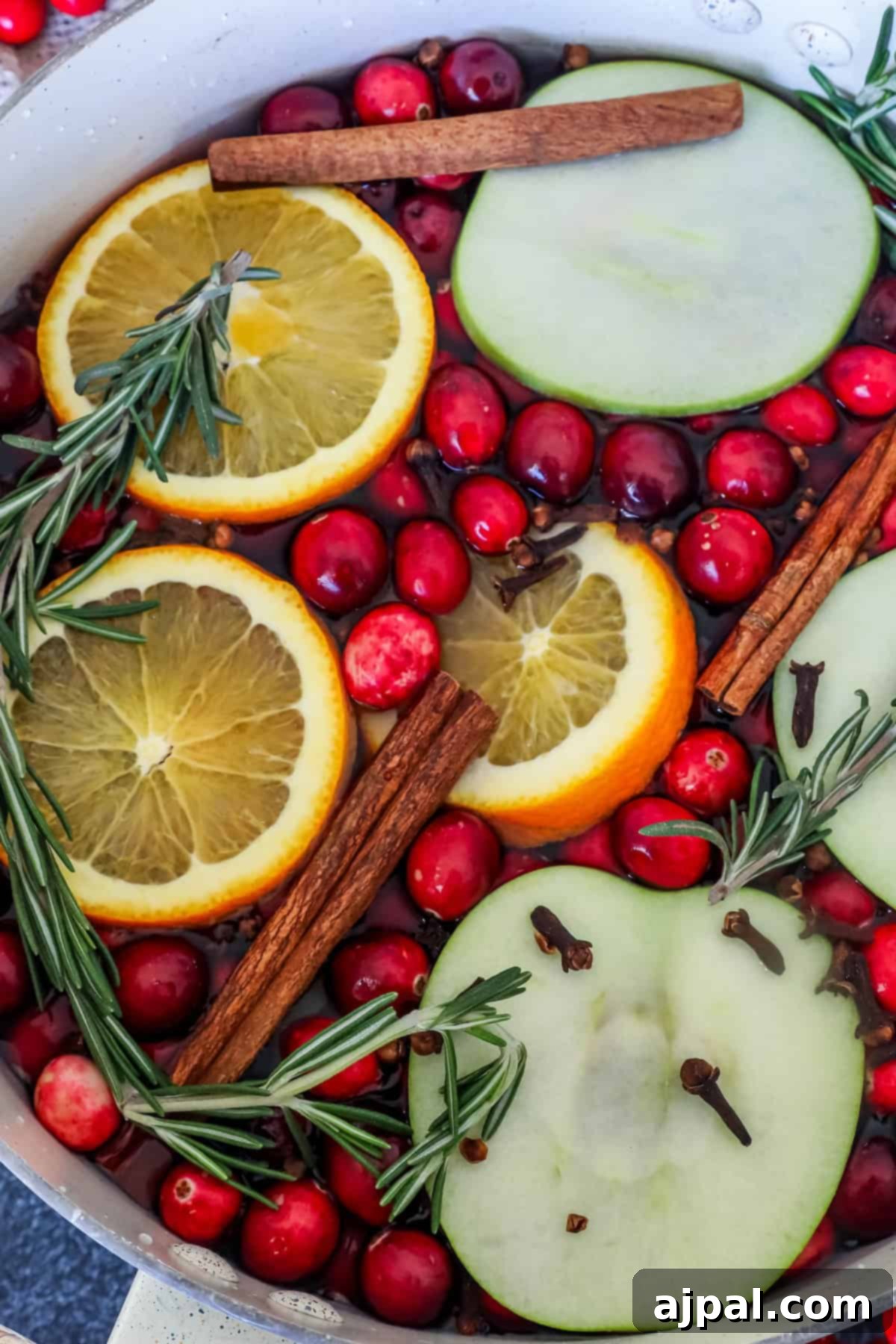A pot of fragrant Christmas potpourri brimming with cranberries, orange and green apple slices, cinnamon sticks, rosemary, and cloves, showcasing a rich and inviting blend of natural scents.