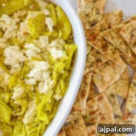 A dish of crumbled feta cheese made into a delightful baked feta dip, accompanied by sliced pepperoncini and pieces of seasoned flatbread.