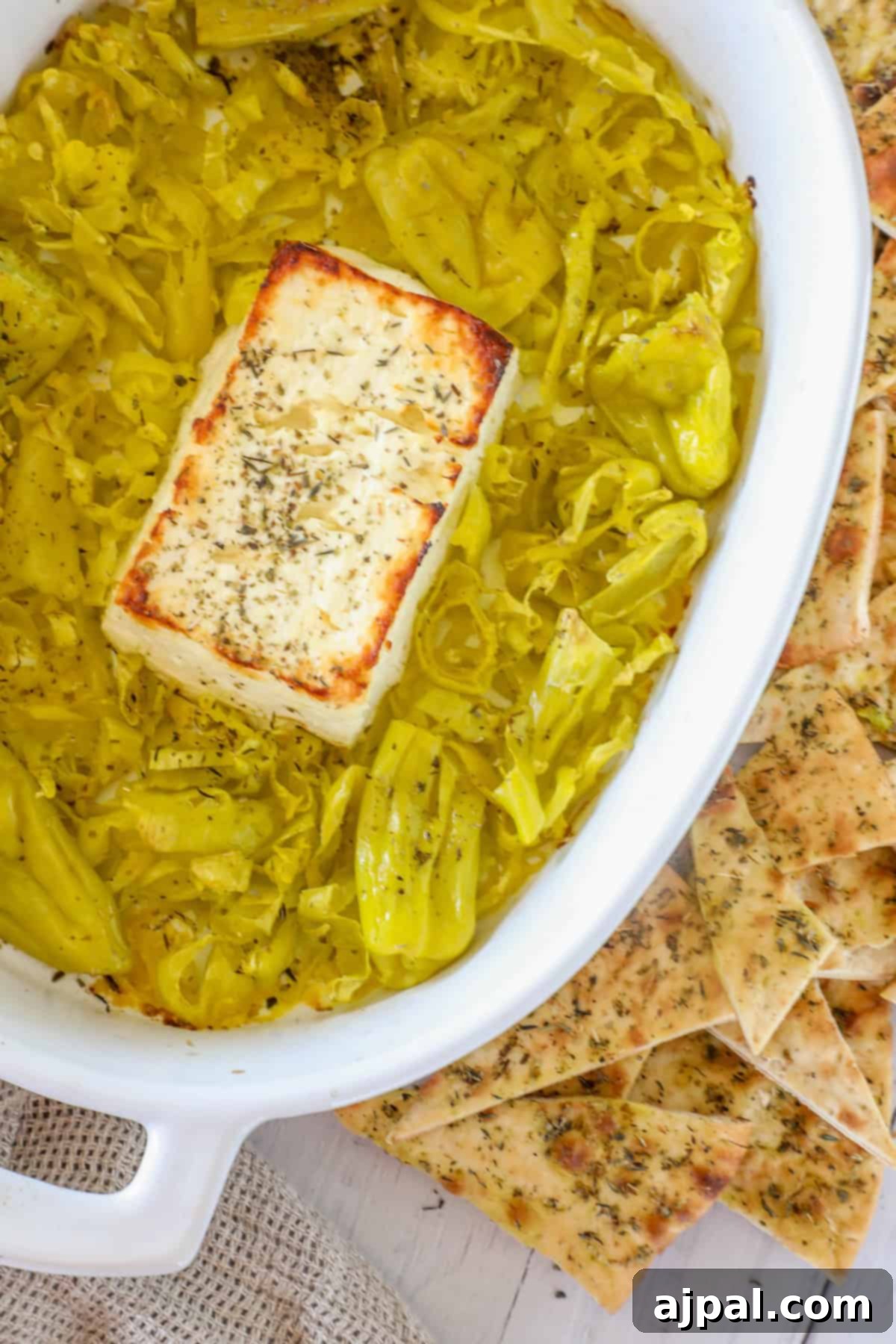 A delicious pepperoncini baked feta dip is served in a dish, featuring sliced pepperoncini and accompanied by herb-topped flatbreads on the side.