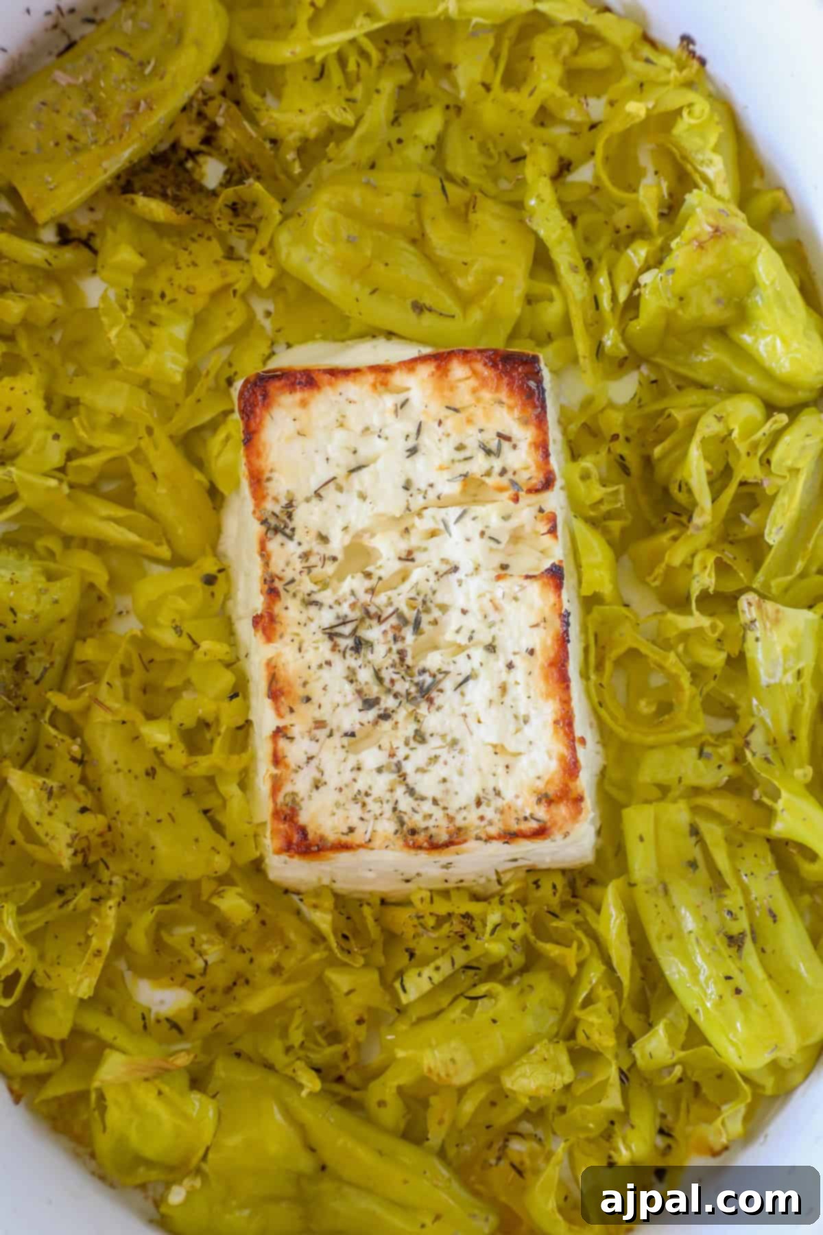 A block of seasoned feta cheese is baked on a bed of sliced pepperoncini in a white dish, creating a delightful baked feta dip.