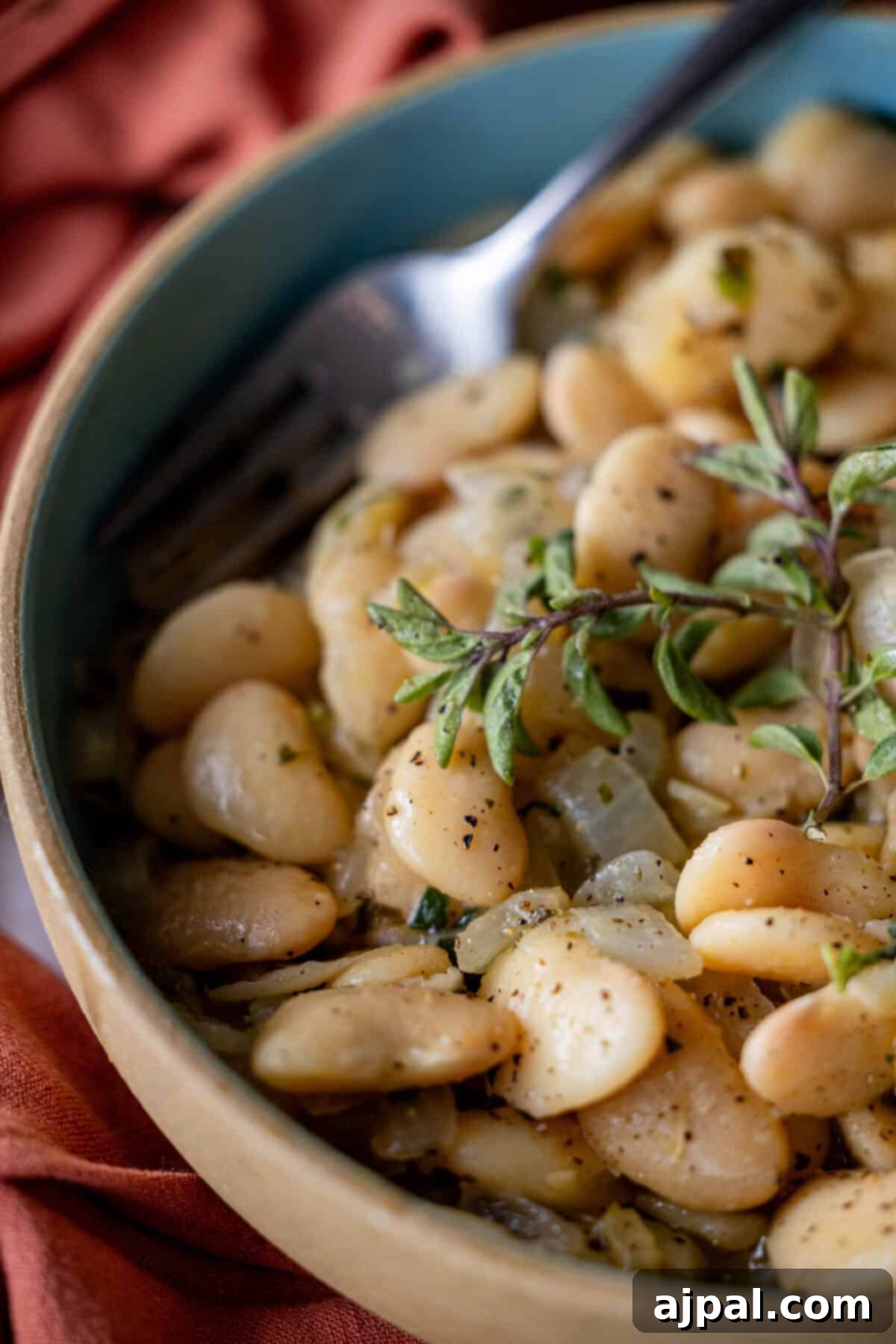 A bowl of seasoned butter beans garnished with fresh herbs and a hint of oregano, with a fork resting inside.