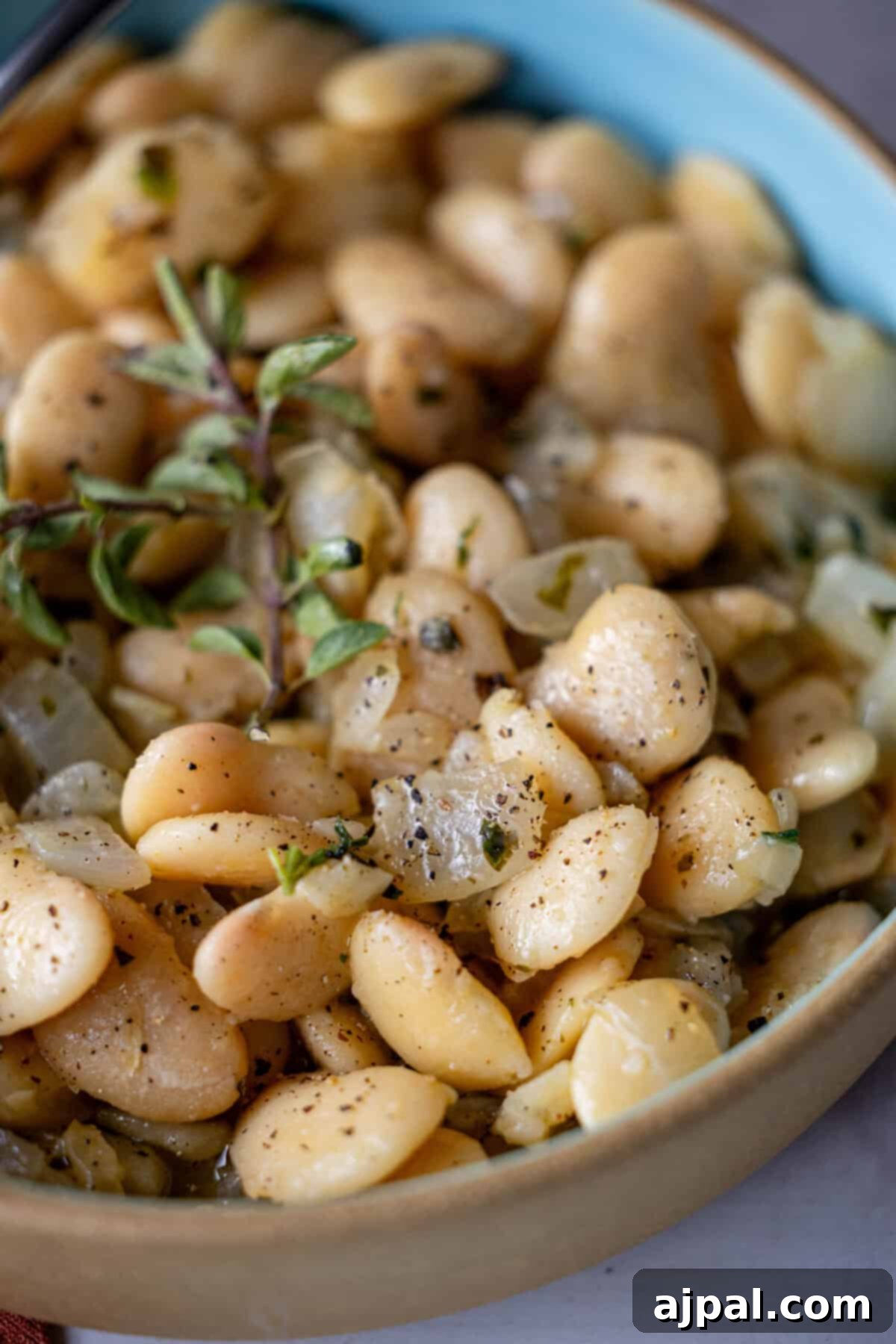 Close-up of a bowl filled with cooked butter beans, delicately garnished with fresh herbs and a hint of oregano, seasoned perfectly with black pepper.