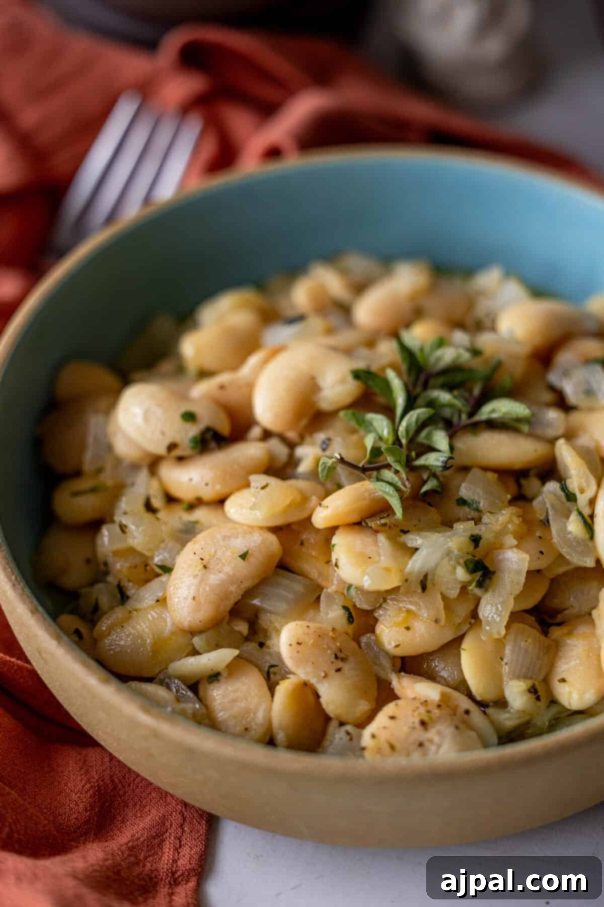 A bowl of cooked butter beans with onions and aromatic herbs, featuring a hint of garlic and garnished with fresh basil leaves.