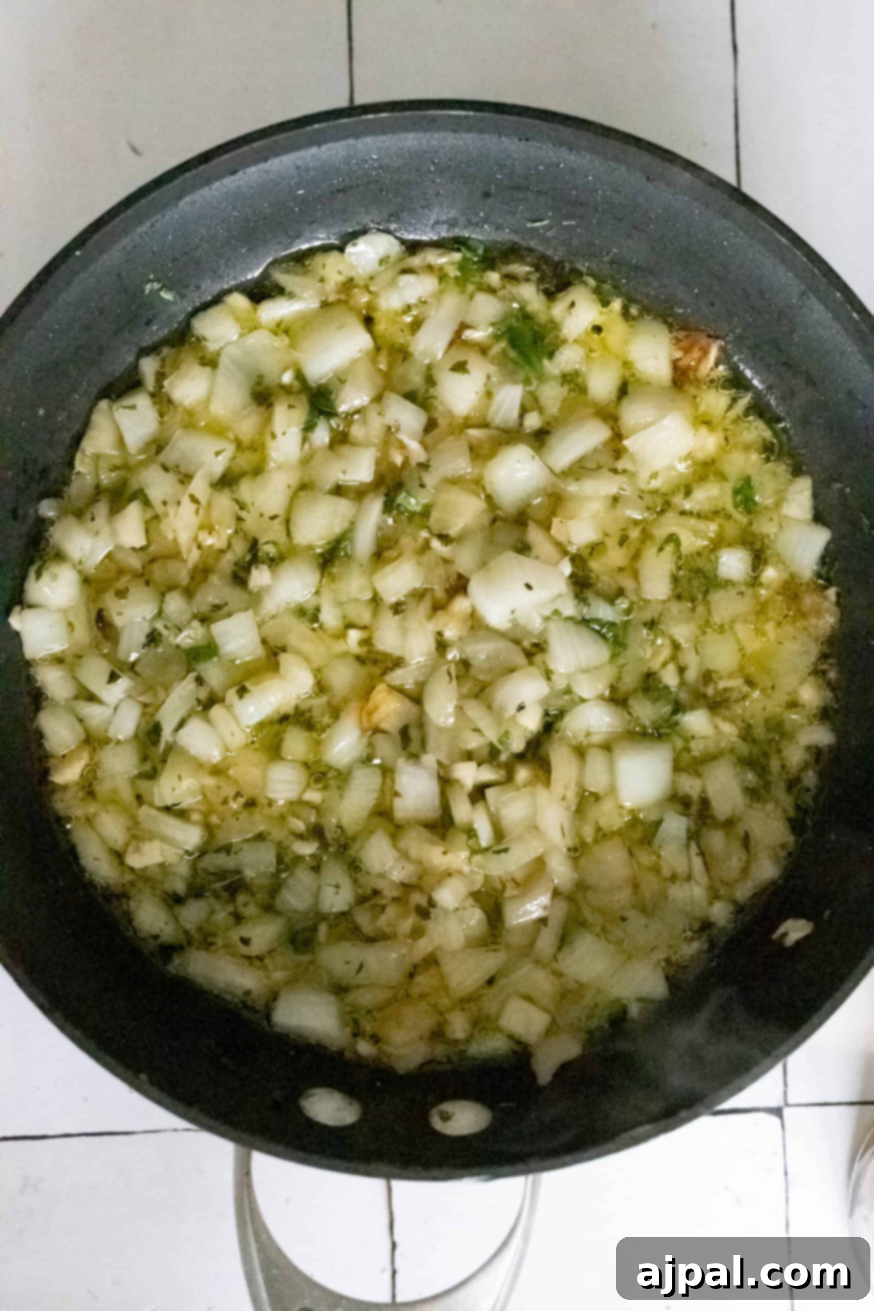 A pan with chopped onions and garlic sautéing in oil on a stove.