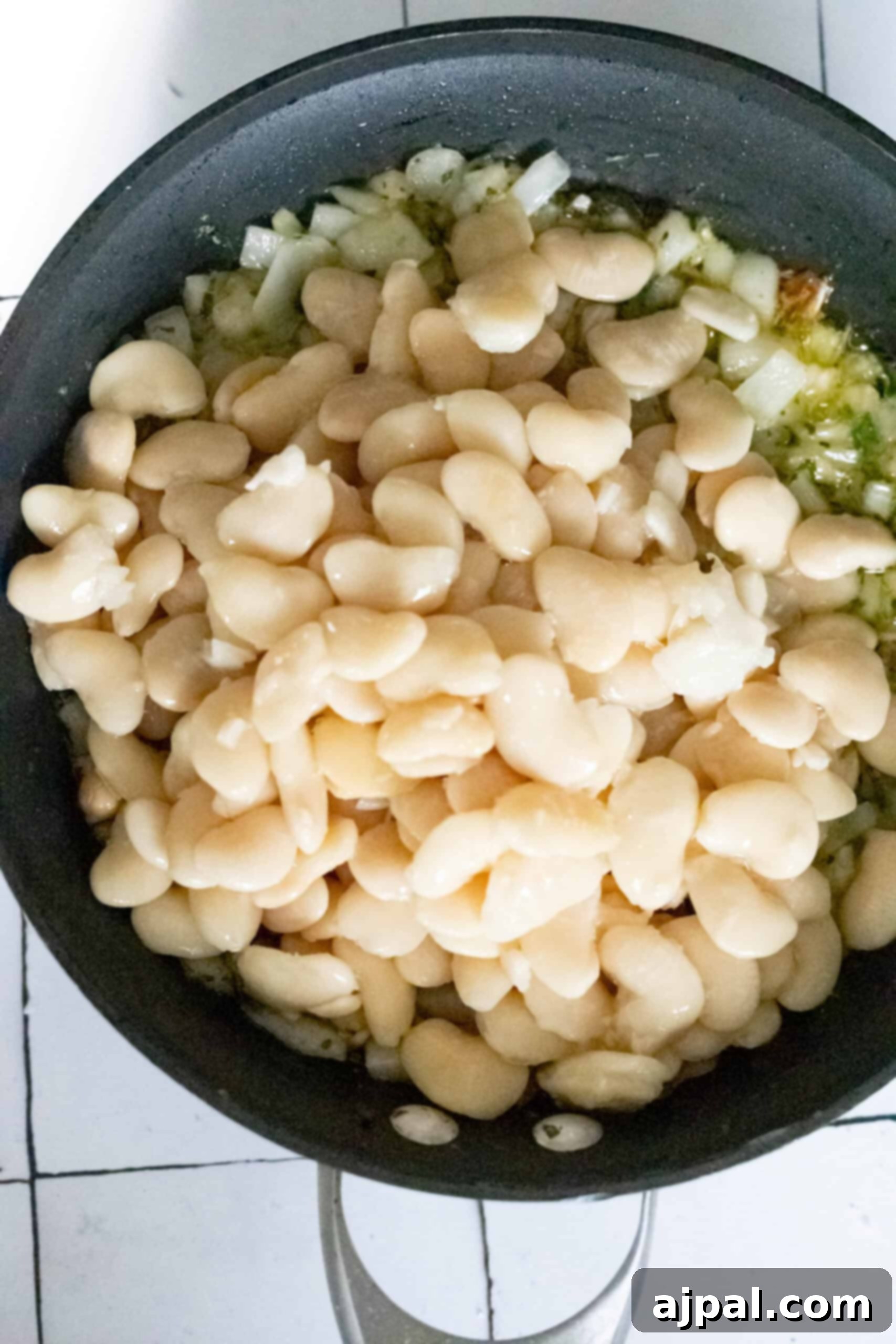 A frying pan sizzles with chopped onions, garlic, and butter beans, creating an aromatic blend.