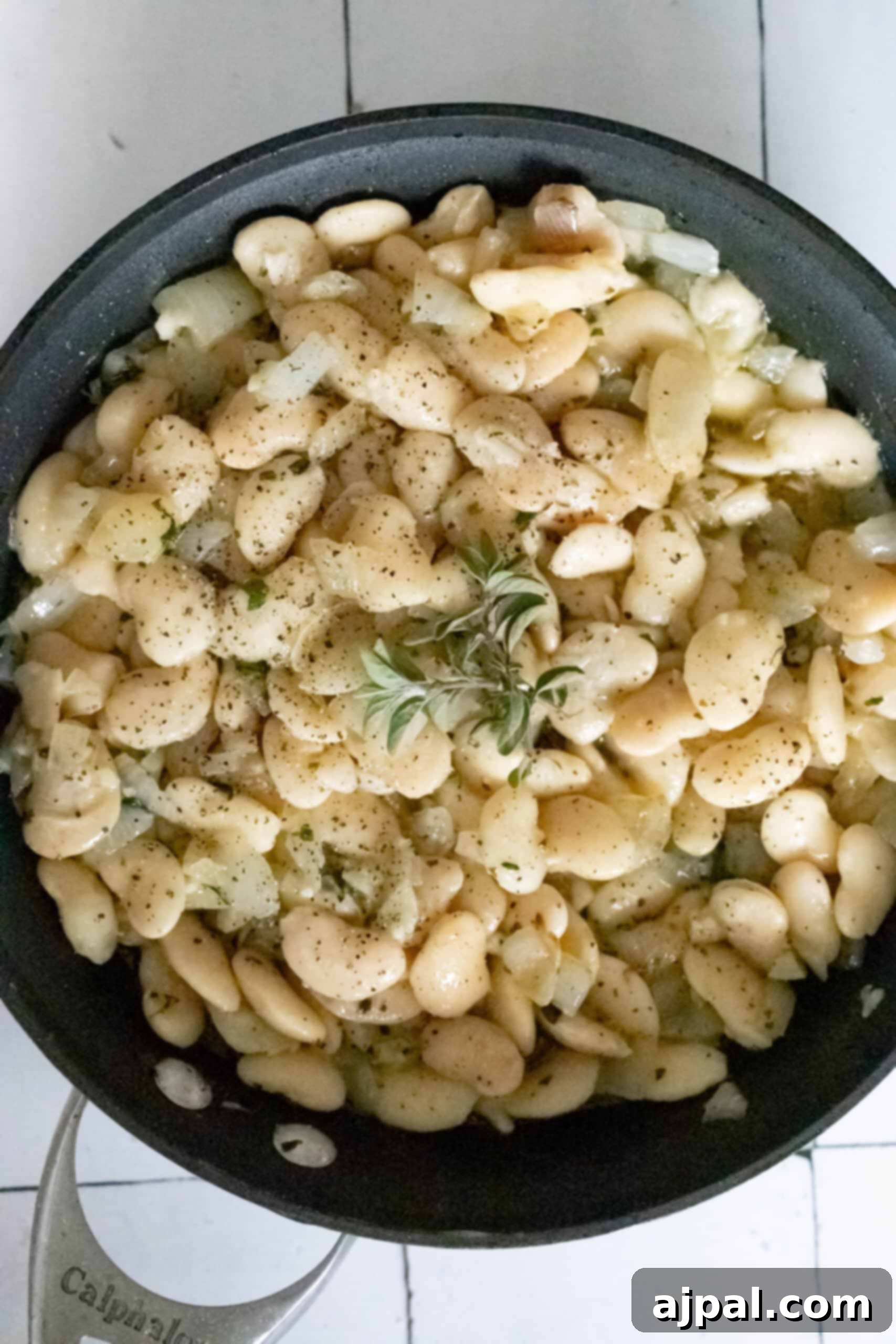 A pan filled with cooked butter beans, seasoned with pepper and topped with fresh herbs and a hint of garlic.