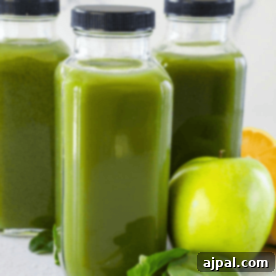 Three bottles of immunity-boosting green juice sit next to a crisp green apple, fresh spinach leaves, and a lemon half on a light surface.