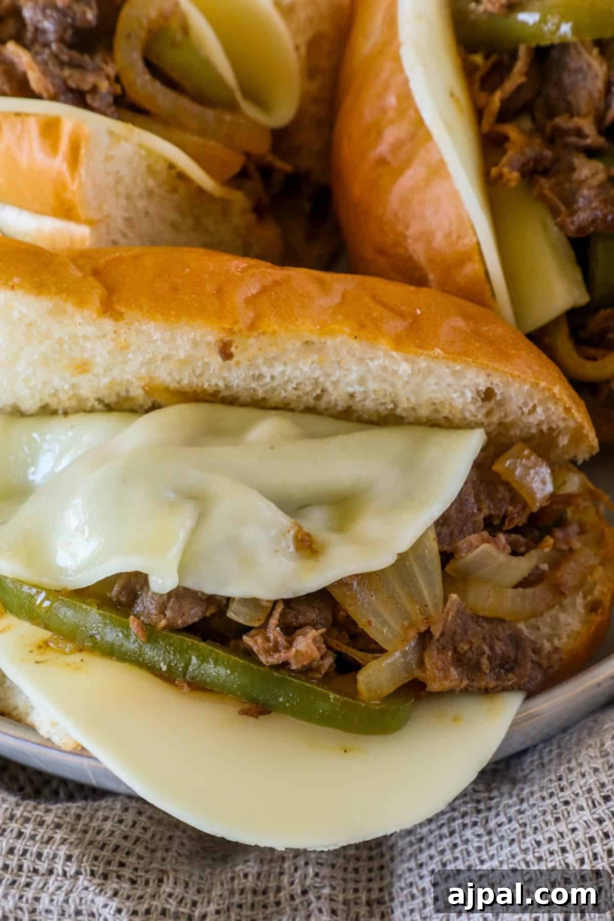 Close-up of a sandwich filled with sliced beef, melted cheese, green peppers, and onions on a bun.