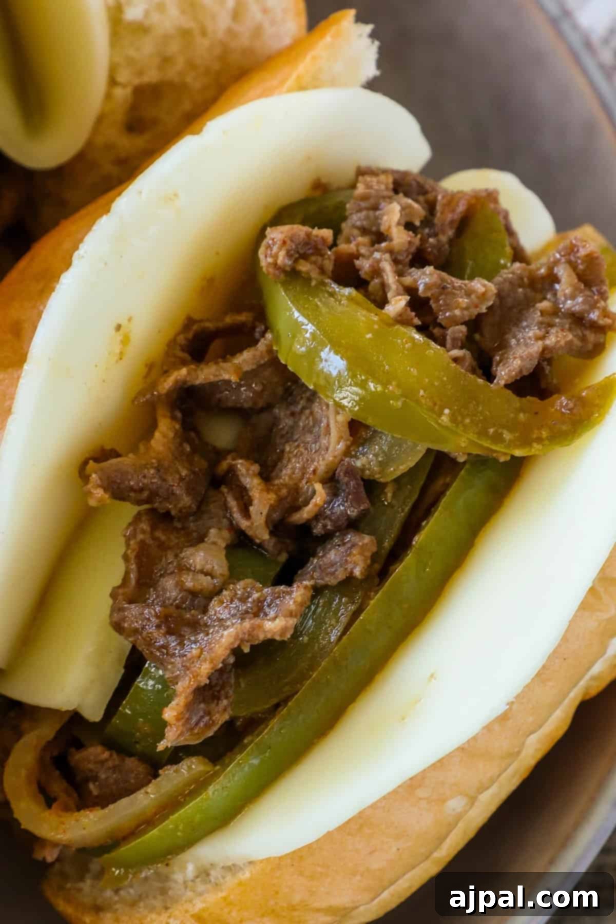 Close-up of a sandwich with melted cheese, sliced grilled beef, and bell peppers on a soft bun.