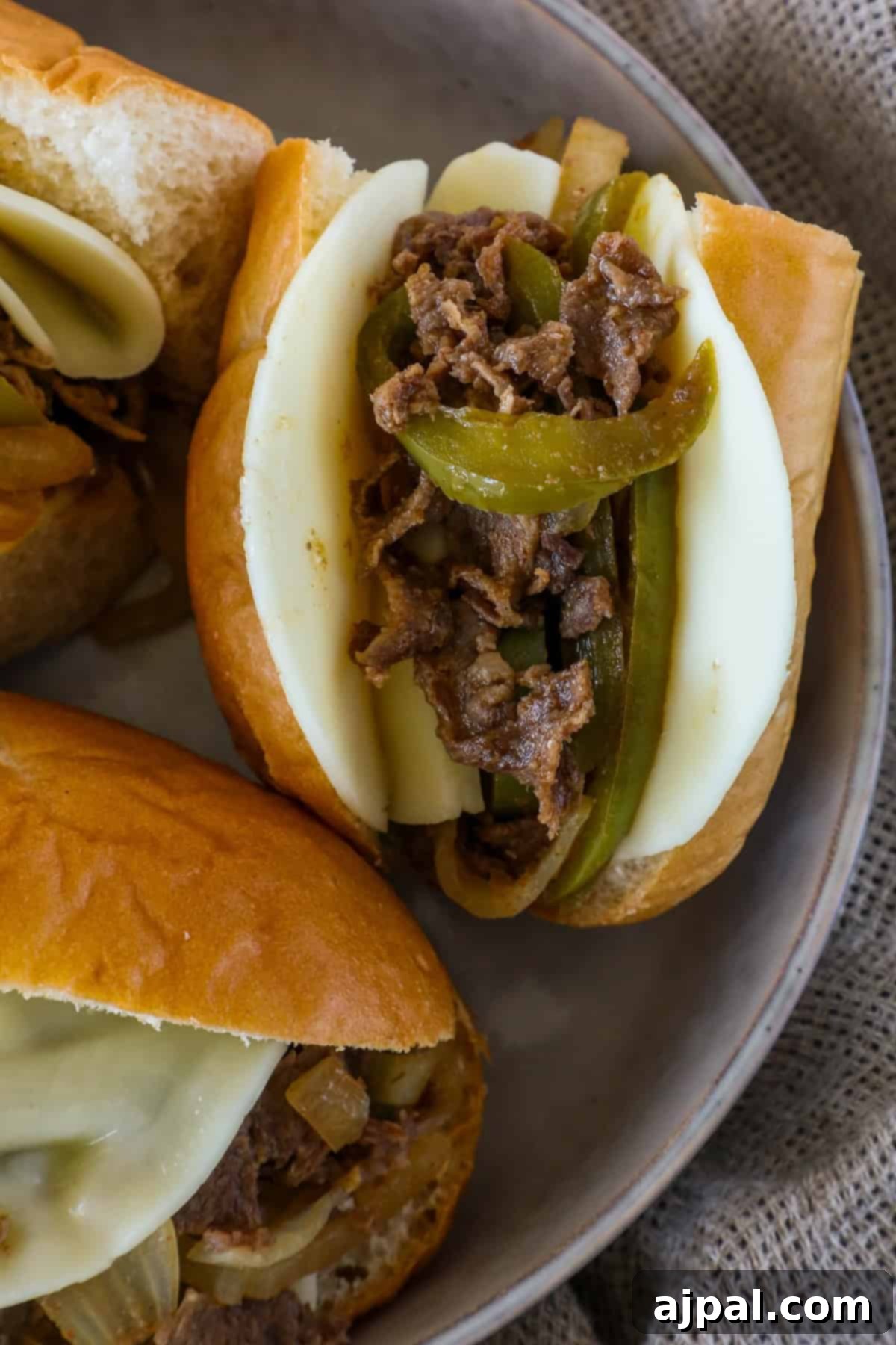 A close-up of a sandwich with sliced beef, melted cheese, green peppers, and onions on a soft bun.