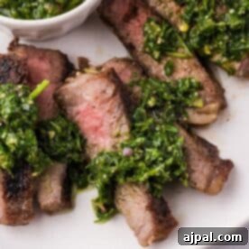 Sliced grilled steak with chimichurri, topped with vibrant green sauce and served on a white plate.