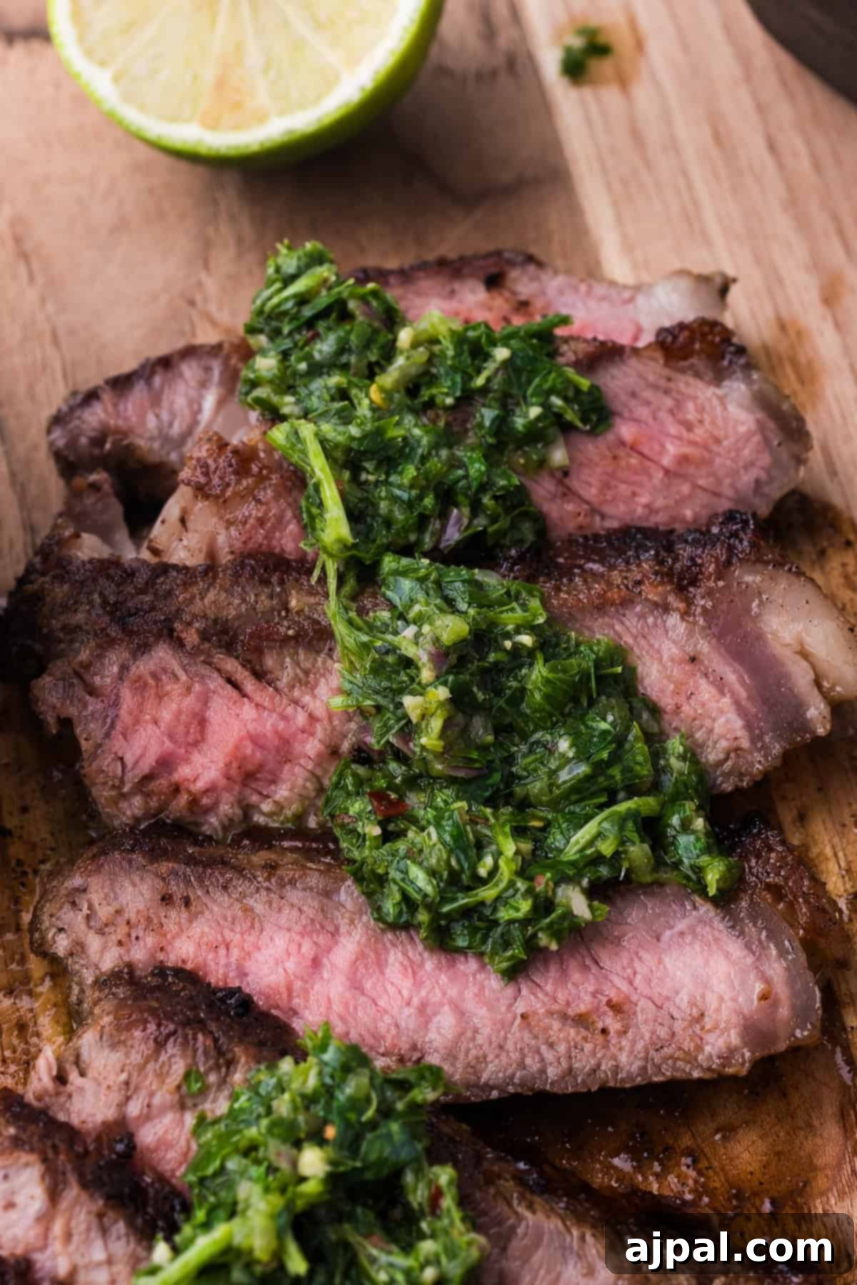 Steak with Chimichurri 4 Sliced medium-rare grilled steak topped with vibrant green herb chimichurri sauce on a wooden board, accompanied by a halved lime in the background. Perfect for those seeking an exquisite steak recipe.