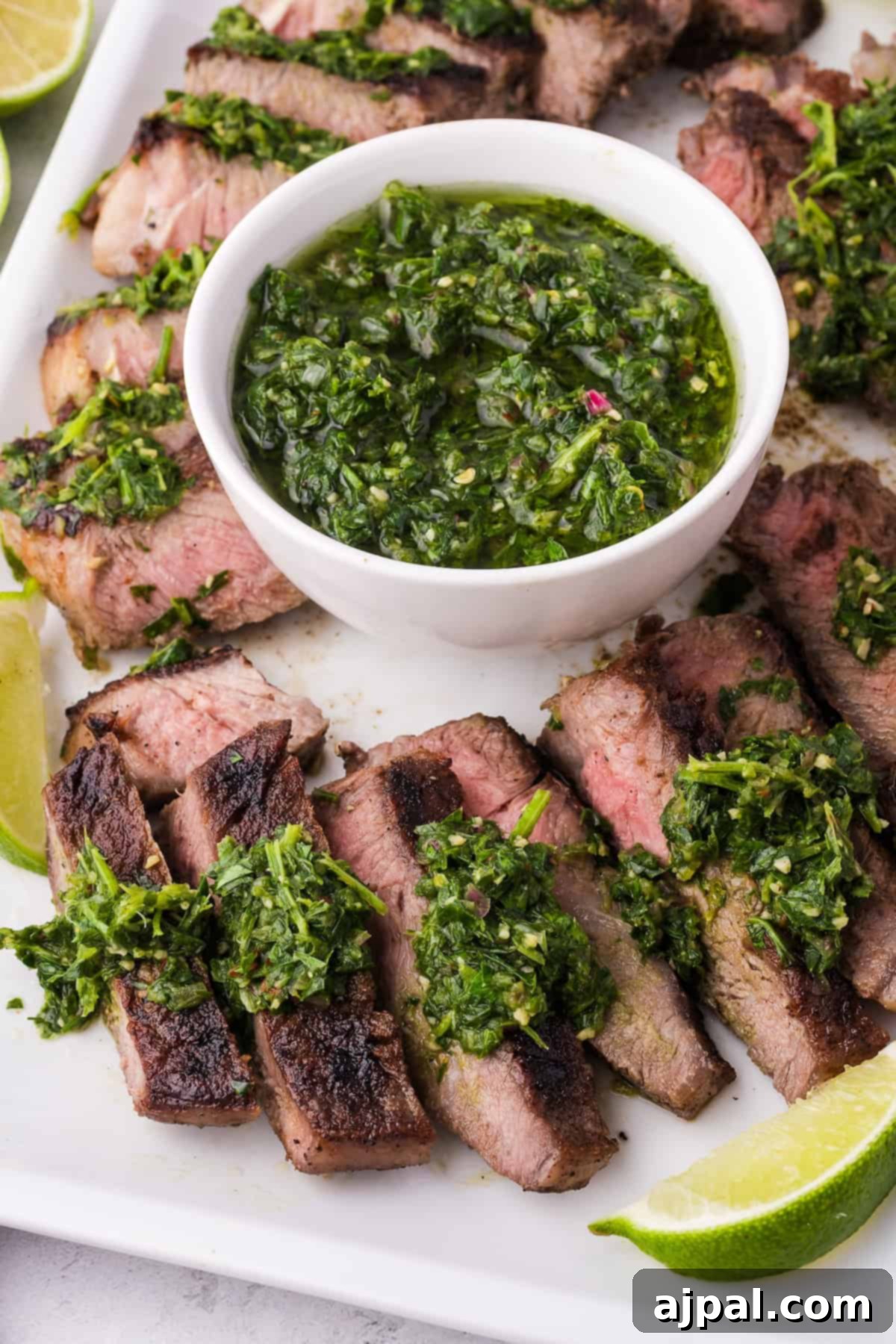 Steak with Chimichurri 5 Sliced steak with a rich chimichurri sauce on a plate, showcasing Argentinian cuisine. A bowl of the vibrant sauce sits at the center, garnished with lime wedges for an extra zing.