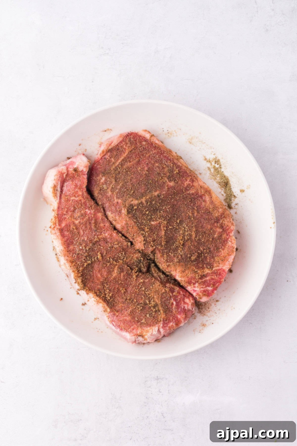 Steak with Chimichurri 6 Two seasoned raw steaks on a white plate, ready to meet their fate as succulent grilled steaks, set against a light background.