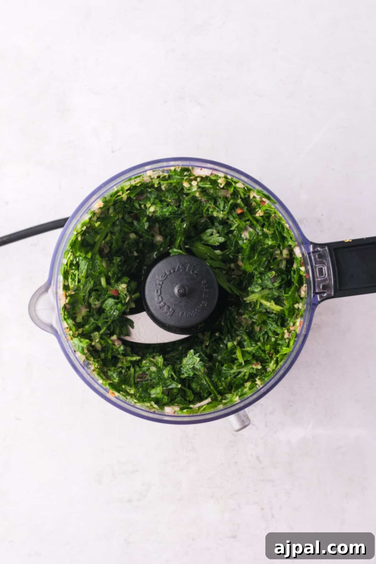 Steak with Chimichurri 7 A food processor with chopped greens inside, perfect for whipping up a fresh chimichurri sauce, viewed from above on a light surface.
