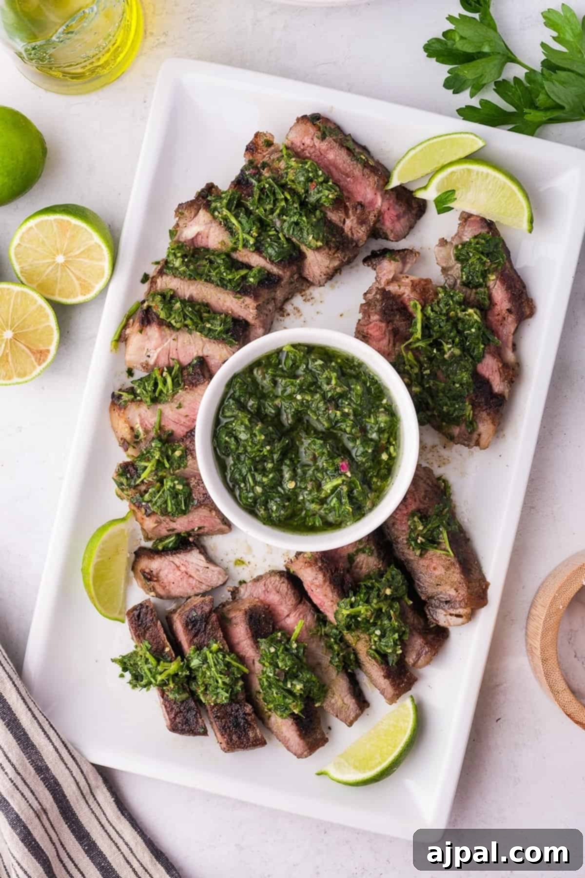 Steak with Chimichurri 9 Sliced grilled steak topped with vibrant chimichurri sauce, elegantly arranged on a rectangular plate and garnished with lime wedges. A small bowl of extra chimichurri sits invitingly at the center, adding a burst of flavor to every bite.