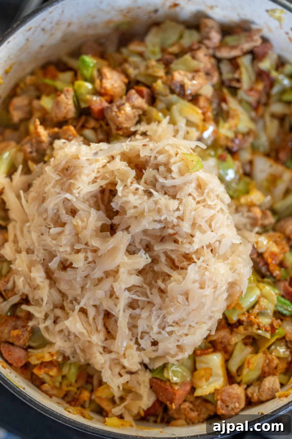In a large pot, a delicious Polish Bigos takes shape, with layers of sauerkraut, cooked sausage, tender cabbage, and various vegetables, creating a hearty and flavorful hunter's stew.