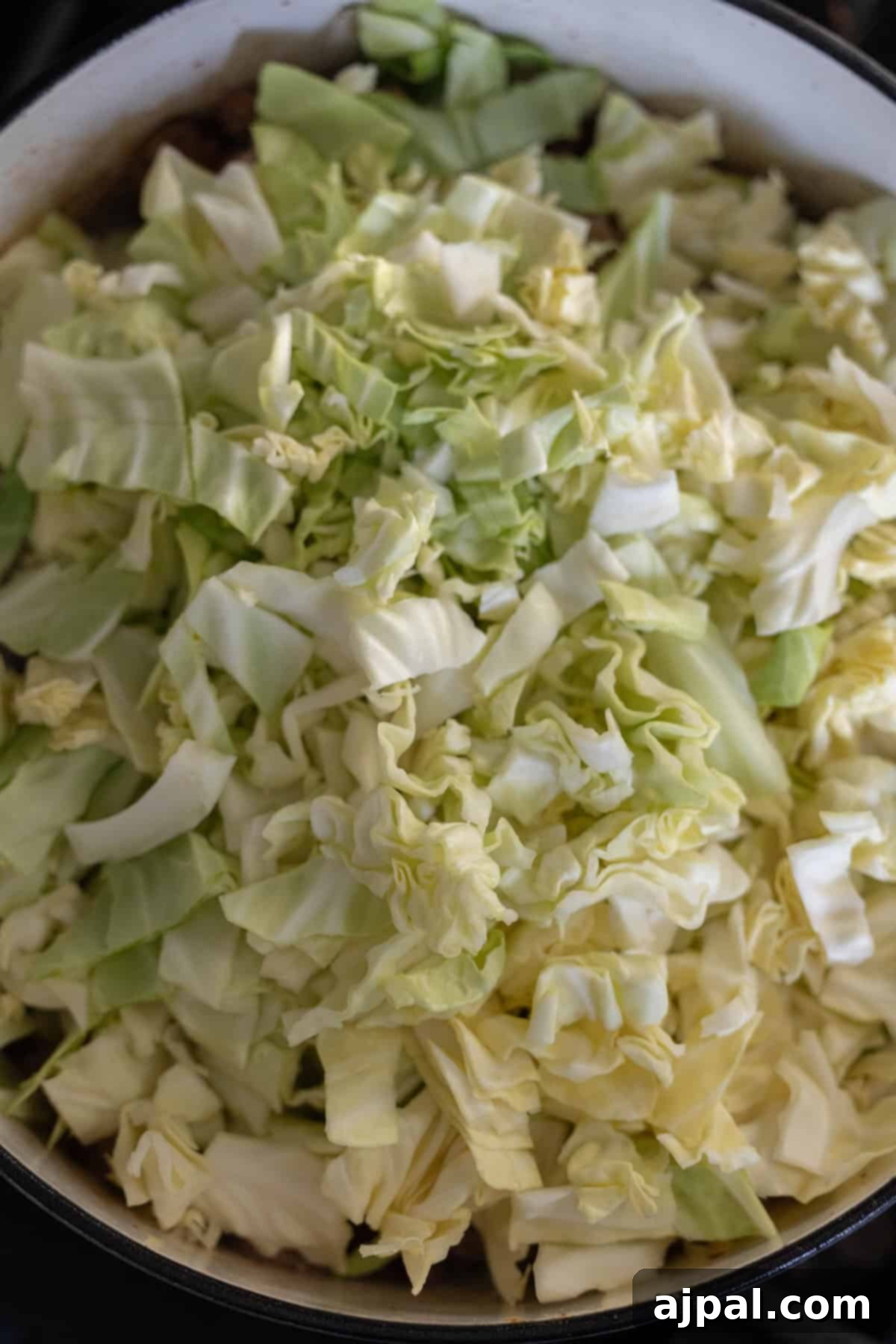 Fresh cabbage, finely shredded, is introduced to the simmering pot, ready to soften and meld with other ingredients for the Bigos stew.