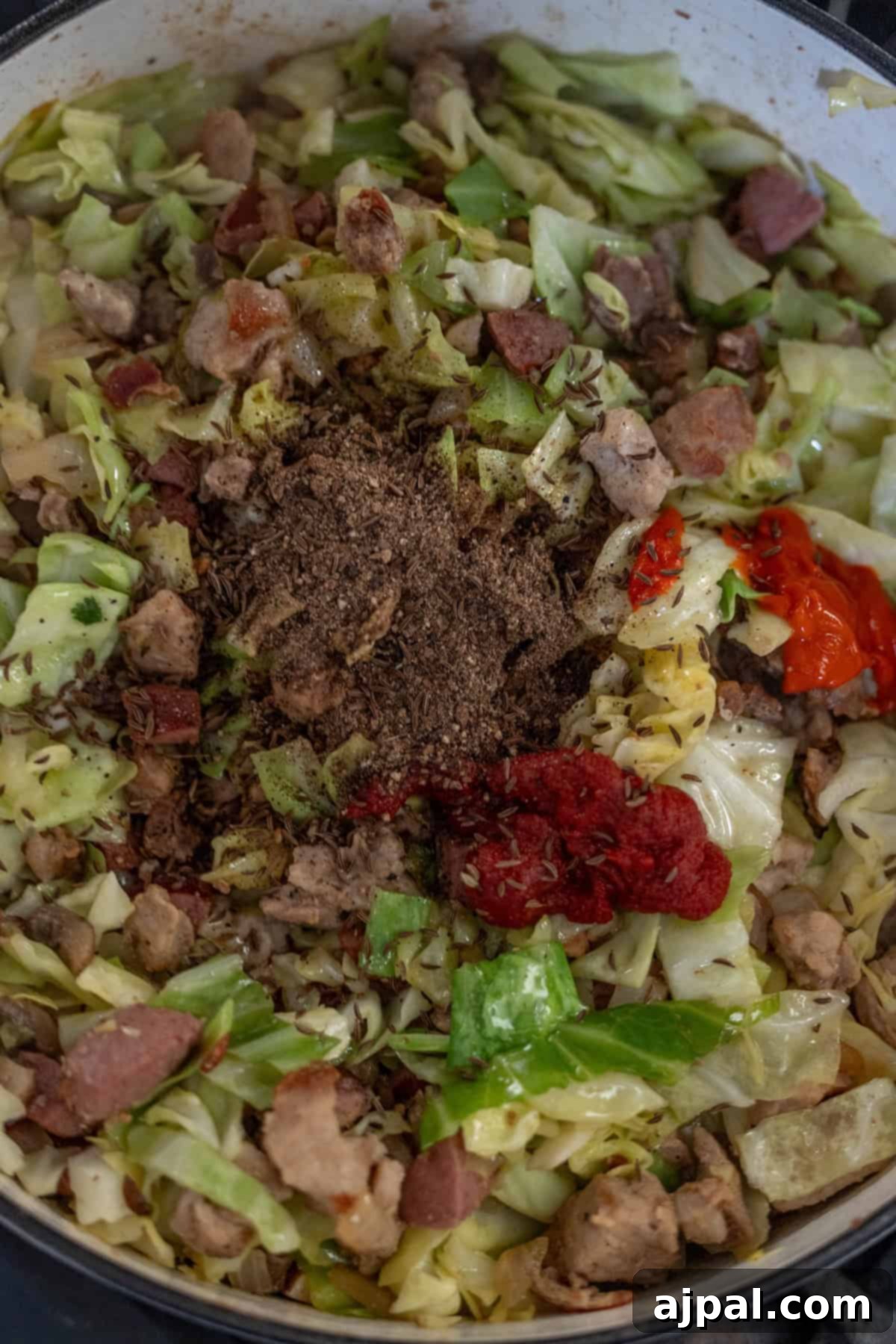 A pot filled with Polish Bigos, featuring chopped cabbage, sausage pieces, ground meat, spices, hot pepper, and tomato paste.