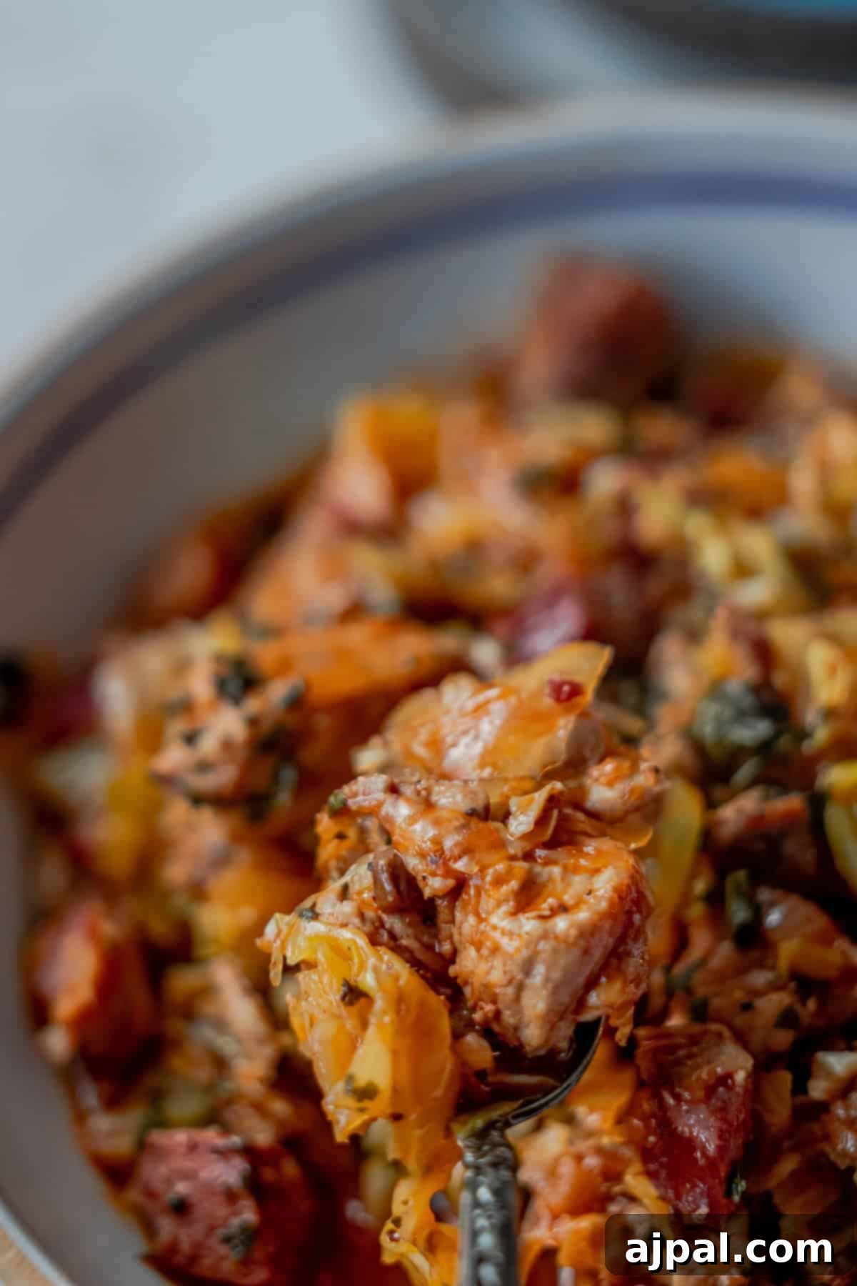 Close-up of a colorful bowl of Polish Bigos, resembling a rich pasta dish, filled with chunks of meat, sliced vegetables, and aromatic herbs.