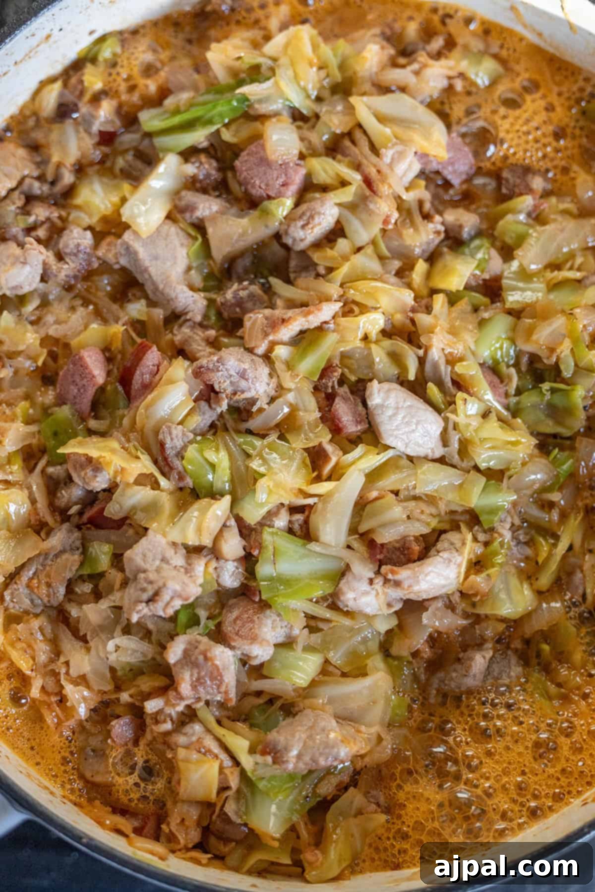 A close-up of a pot containing Bigos, the traditional Polish Hunter's Stew, made with cabbage, sliced meat, and sausages in a rich, simmering broth.