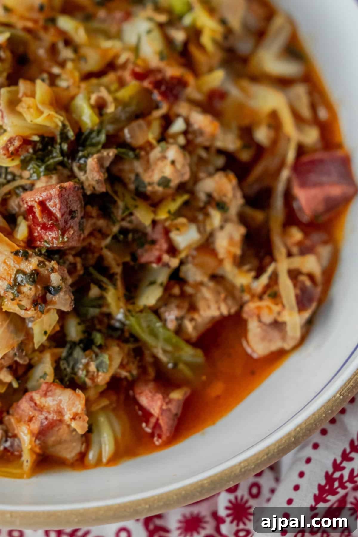 A close-up of a rustic Polish Bigos, known as Hunter's Stew, featuring generous chunks of meat, mixed vegetables, and fragrant herbs in a thick, reddish sauce, presented in a white bowl on a festive tablecloth.