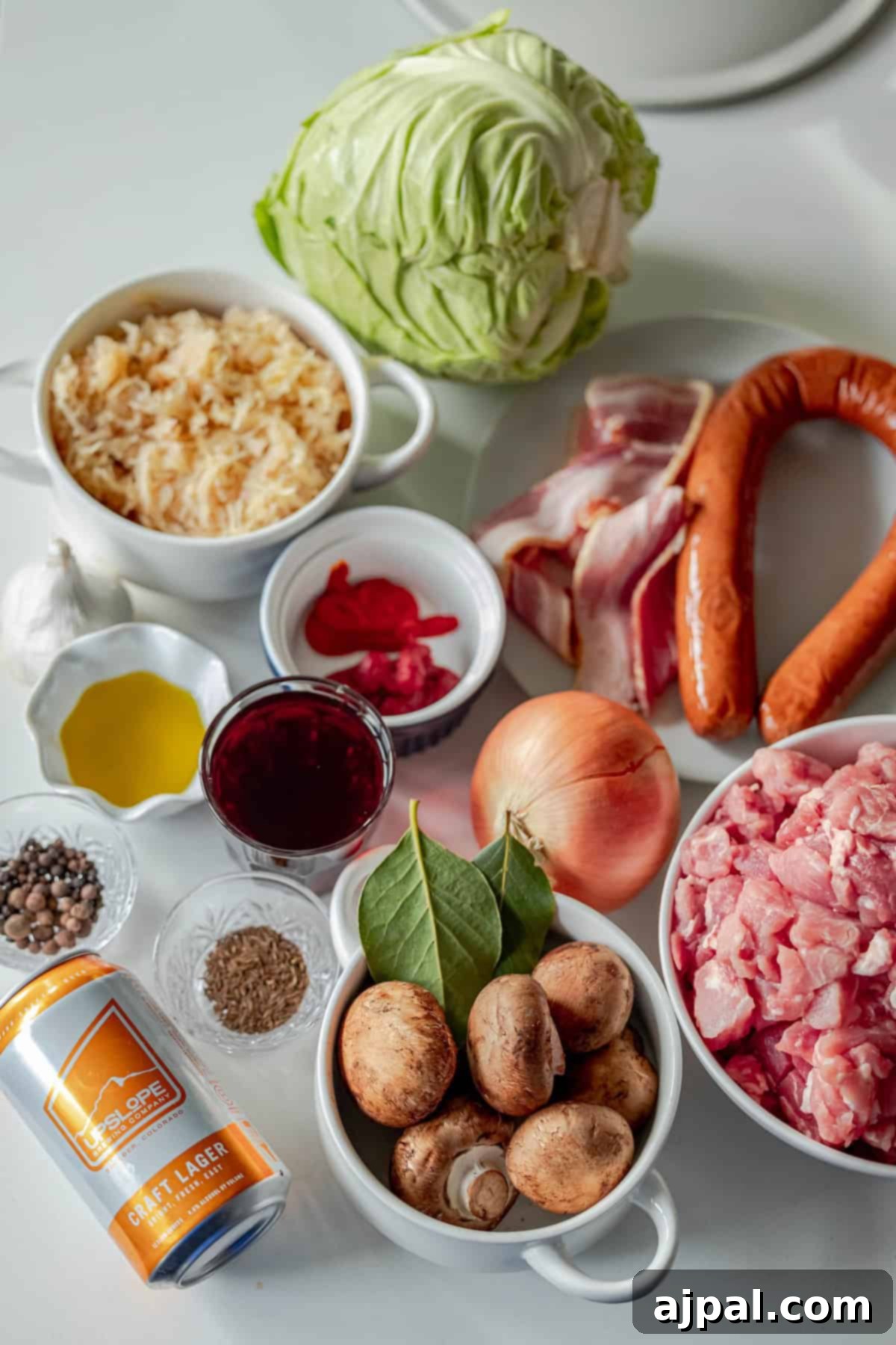 A savory spread of ingredients like cabbage, rice, bacon, and various sausages, ready to be transformed into a traditional Polish Bigos stew with pork pieces and peppercorns, alongside a glass of red liquid for deep flavor.