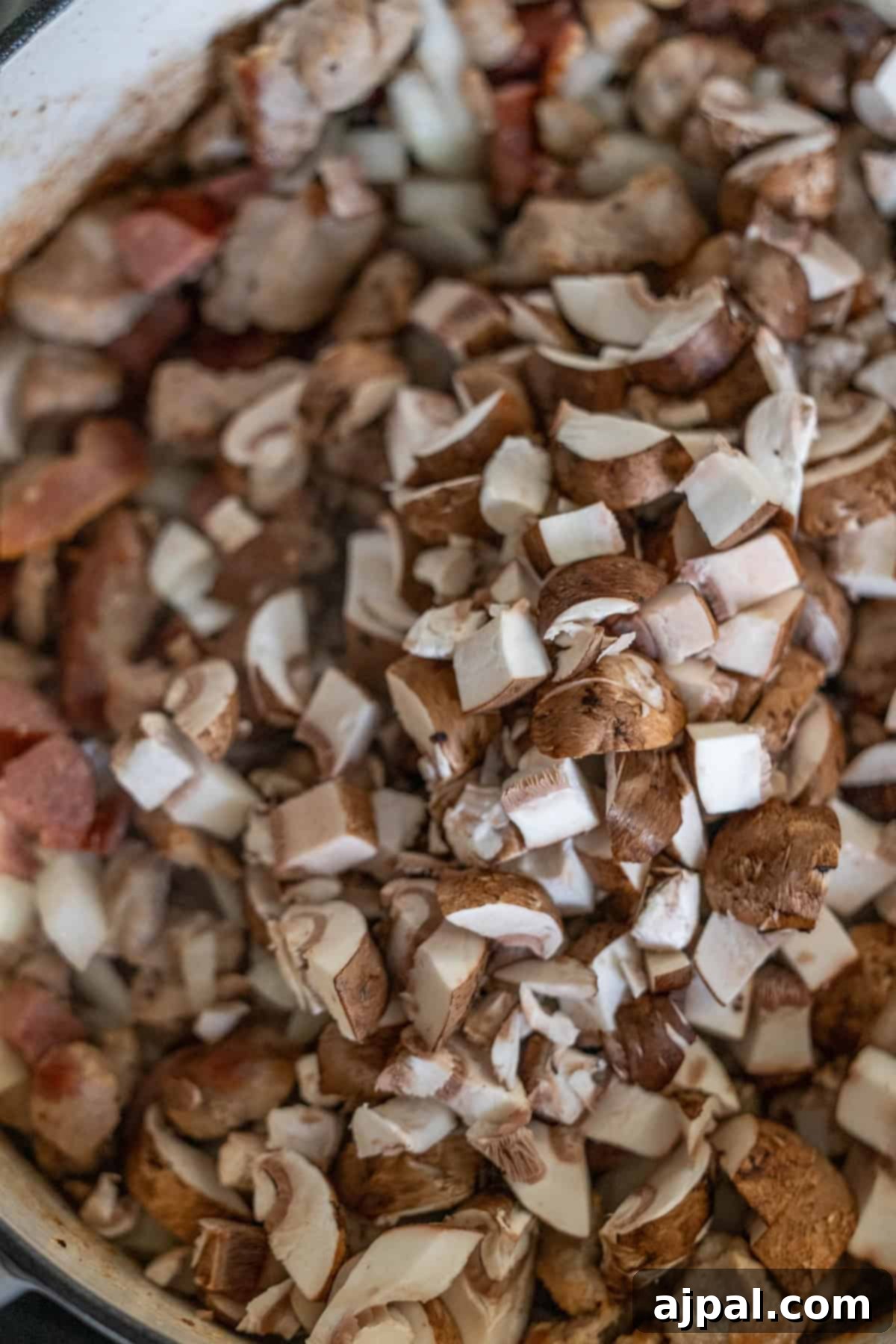 Chopped mushrooms and crispy bacon pieces sizzling in a pan, forming the savory base for a traditional hunter's stew that promises rich flavors.