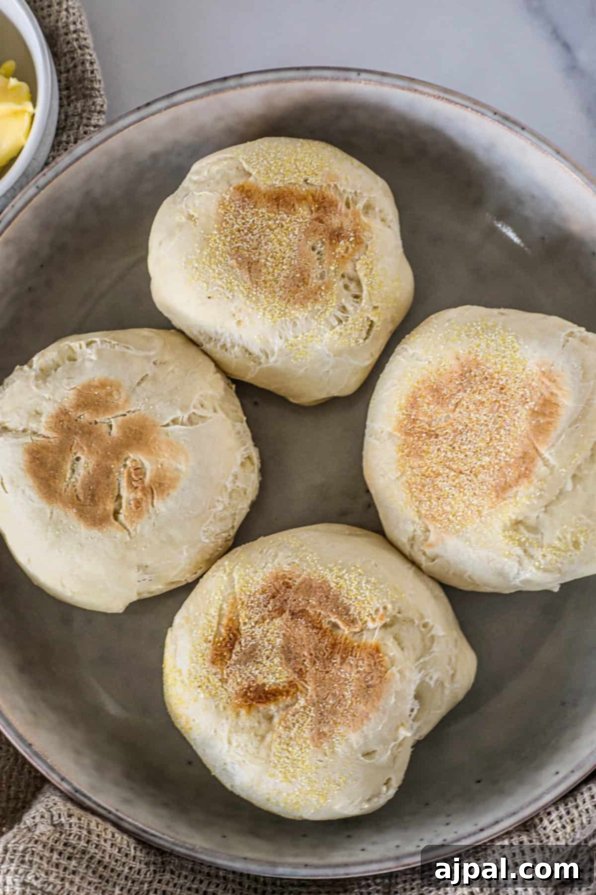 Four homemade English muffins on a round gray plate.