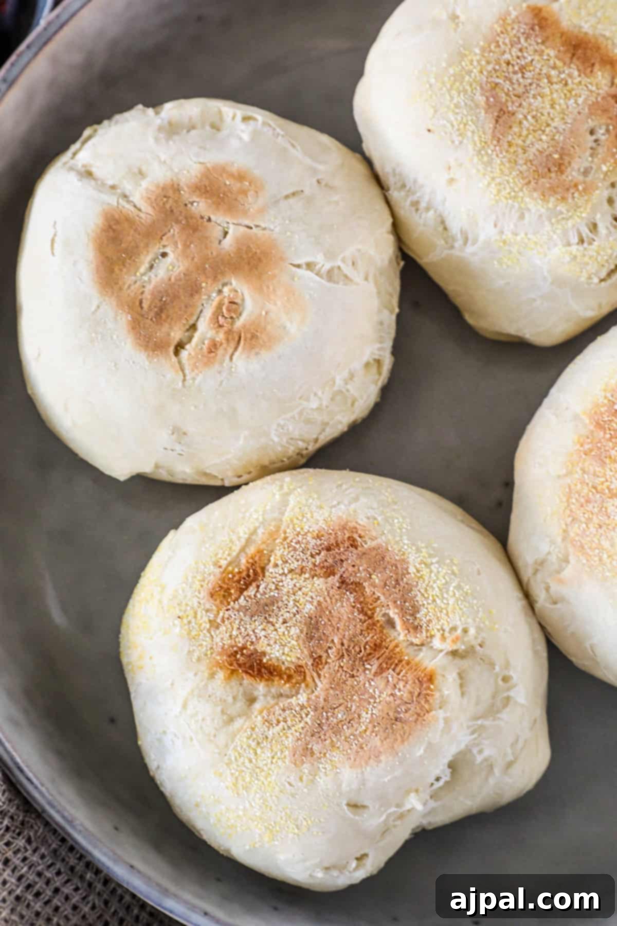 Four baked English muffins with golden brown tops on a gray plate.