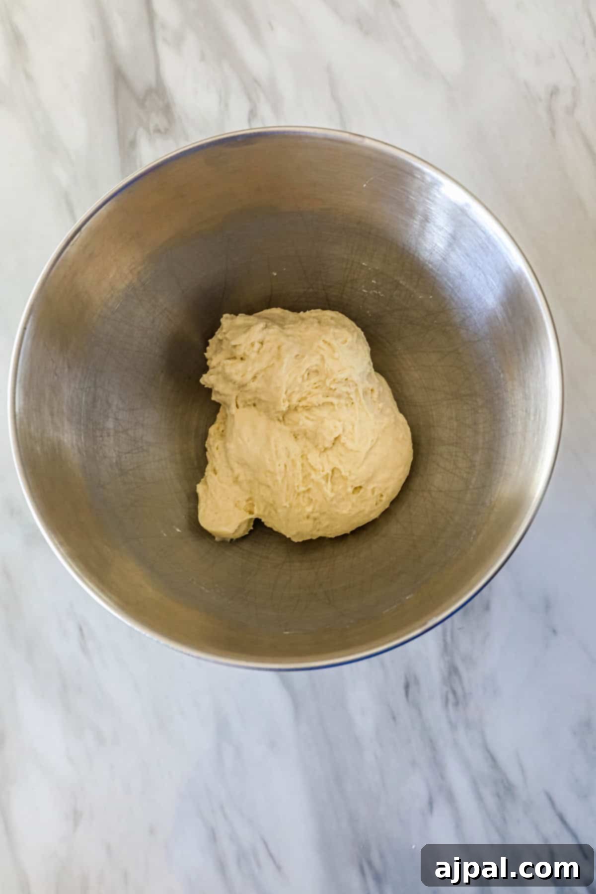 Ball of dough in a metal mixing bowl on a marble countertop.