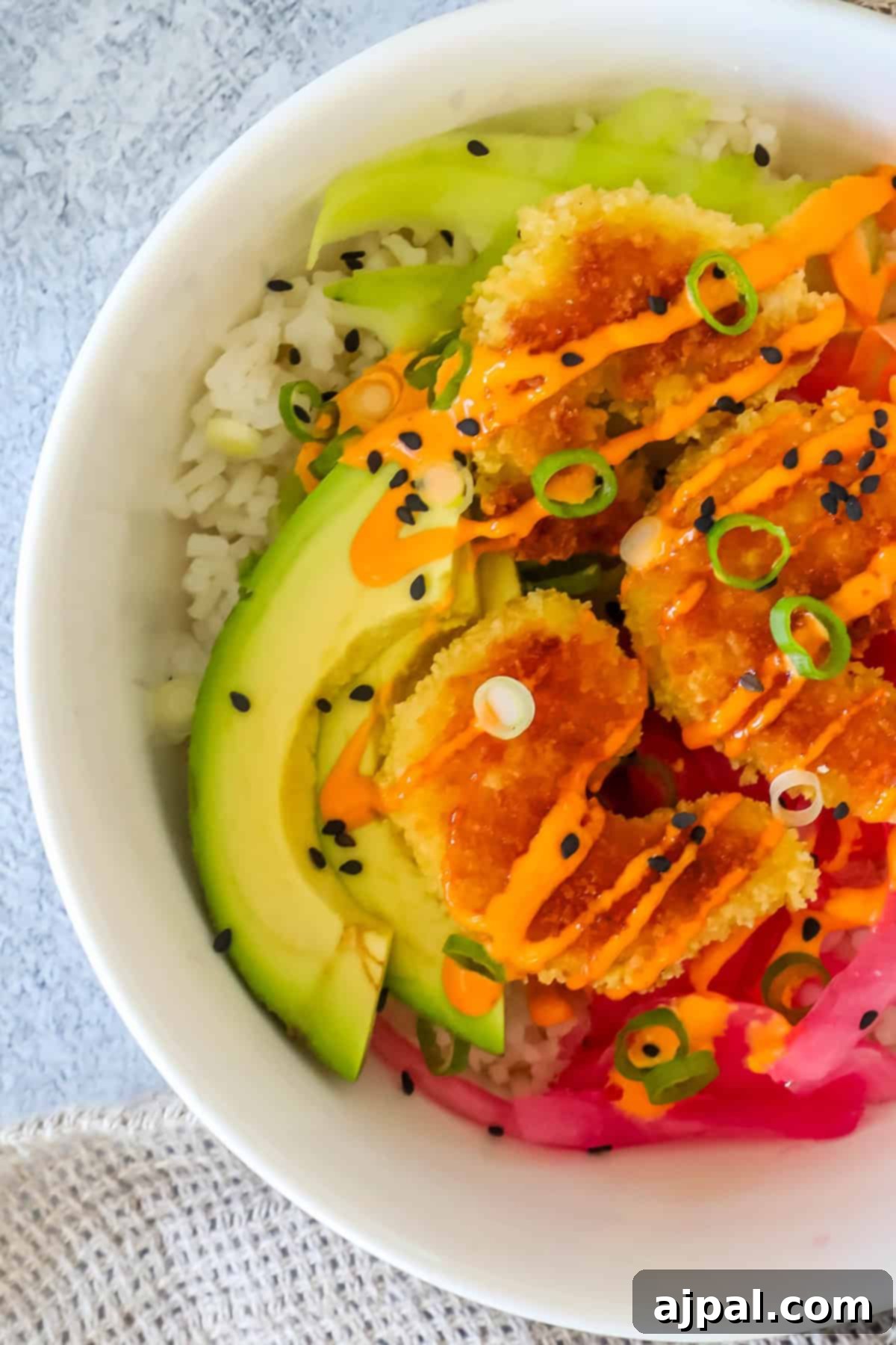 Golden Crispy Shrimp Rice Bowls 2 A vibrant bowl of crispy shrimp rice featuring golden-brown shrimp, creamy avocado slices, and a colorful array of fresh vegetables, drizzled with a rich orange sauce, garnished with green onions and black sesame seeds.