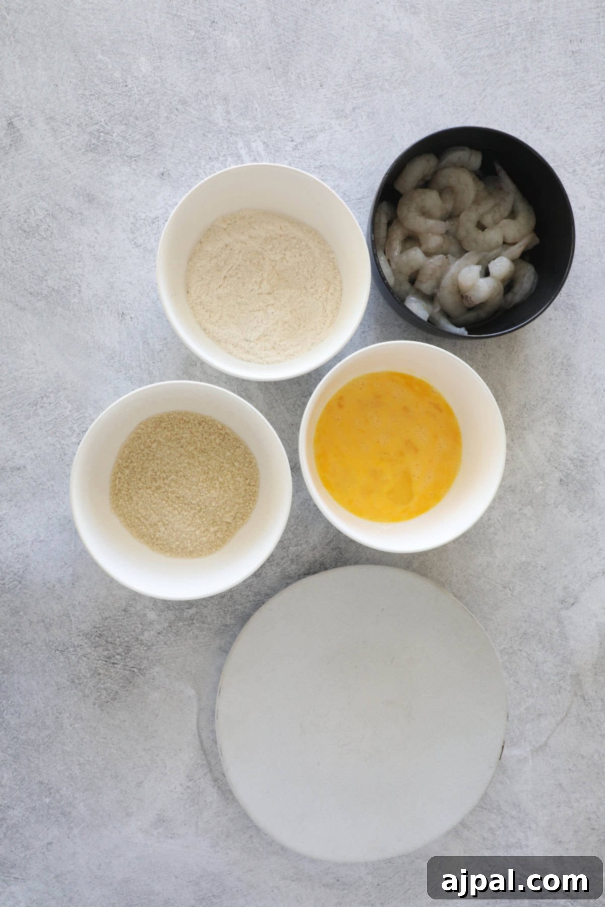 Golden Crispy Shrimp Rice Bowls 5 Bowls containing flour, breadcrumbs, beaten egg, and raw shrimp are arranged on a gray surface, ready for a cooking preparation.