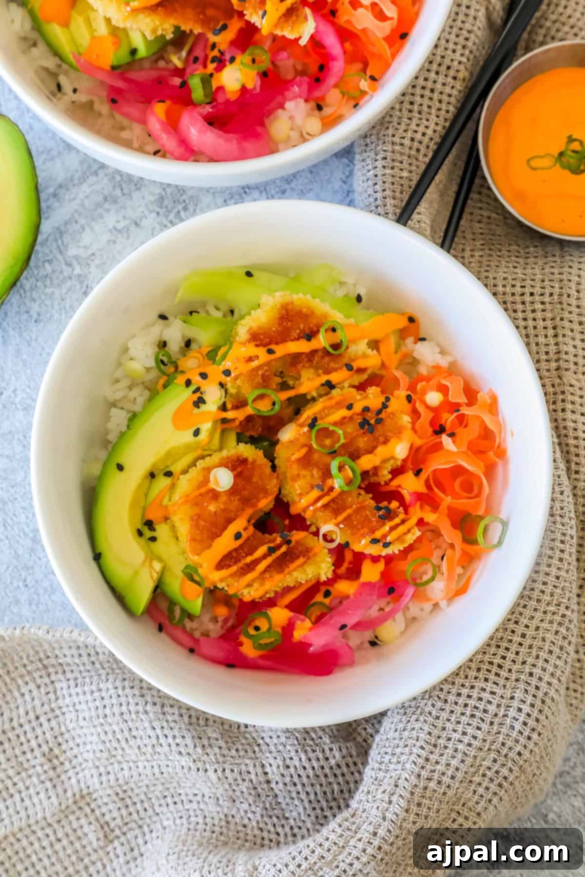 Golden Crispy Shrimp Rice Bowls 8 A beautifully assembled rice bowl, generously topped with an array of fresh ingredients: perfectly sliced avocado, vibrant pickled vegetables, and golden-brown crispy breaded shrimp, all elegantly garnished with black sesame seeds and fresh green onions.
