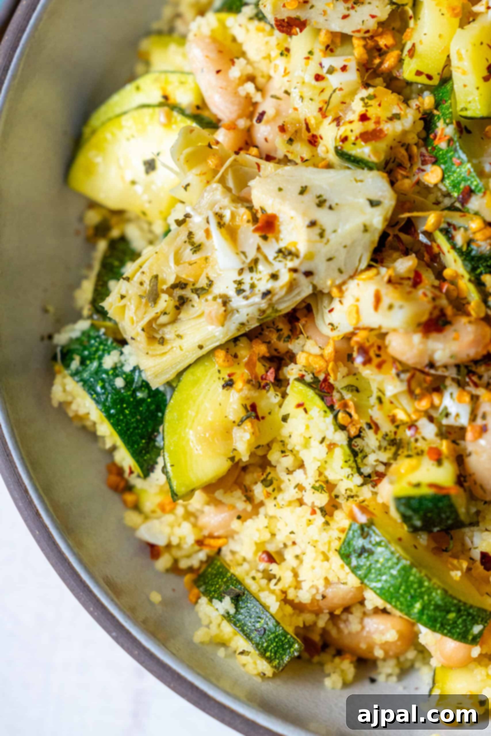 Spicy Mediterranean Cured Lemon Couscous 2 A vibrant bowl of spicy Mediterranean preserved lemon couscous, featuring fluffy couscous, bright yellow preserved lemon pieces, green zucchini wedges, and succulent artichoke hearts. The dish is garnished with fresh herbs and a sprinkle of red pepper flakes, highlighting its rich textures and inviting colors. Perfect for a healthy, comforting vegan dinner.