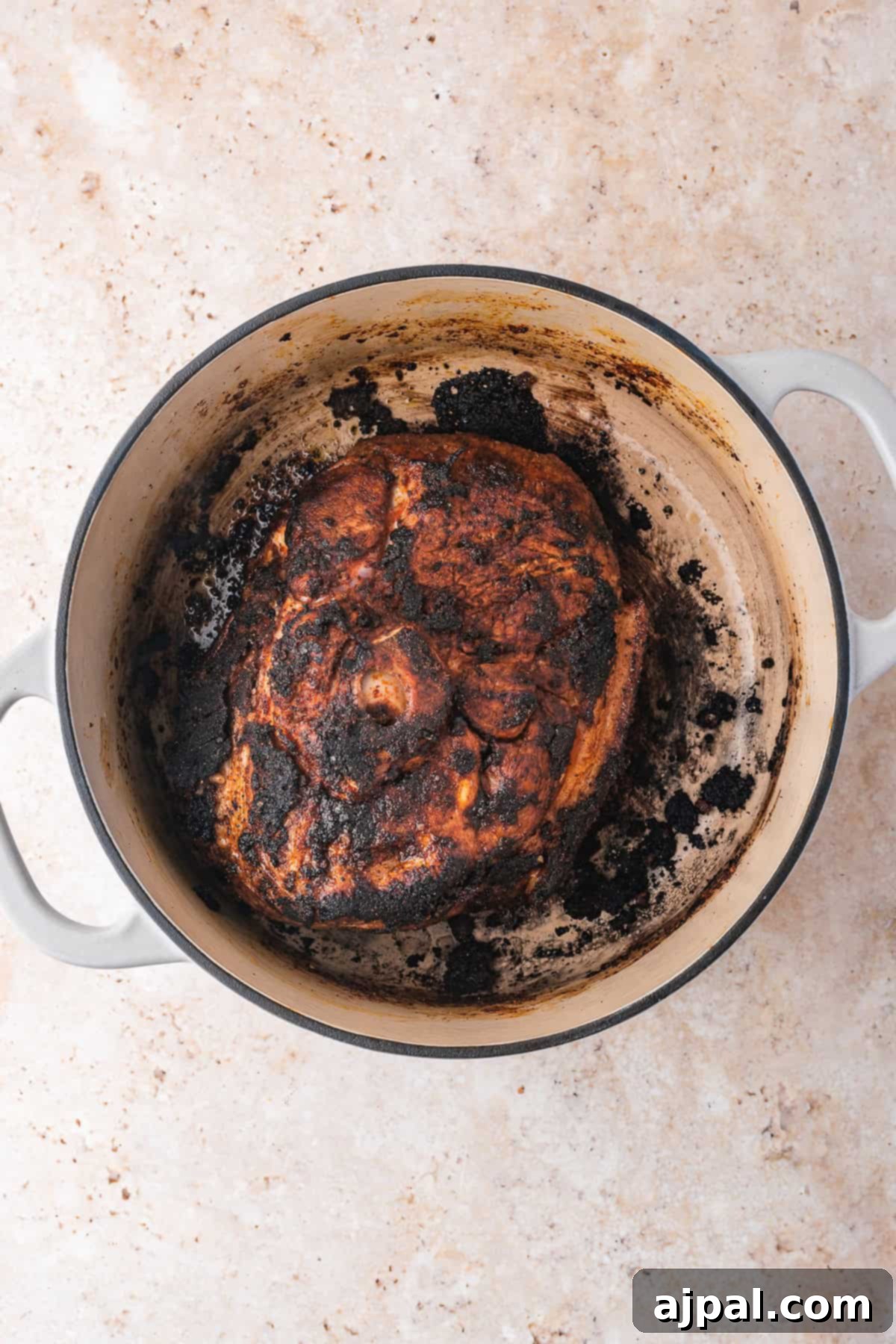 A burnt roast sits in a Dutch oven on a light marble surface, embodying rustic charm.